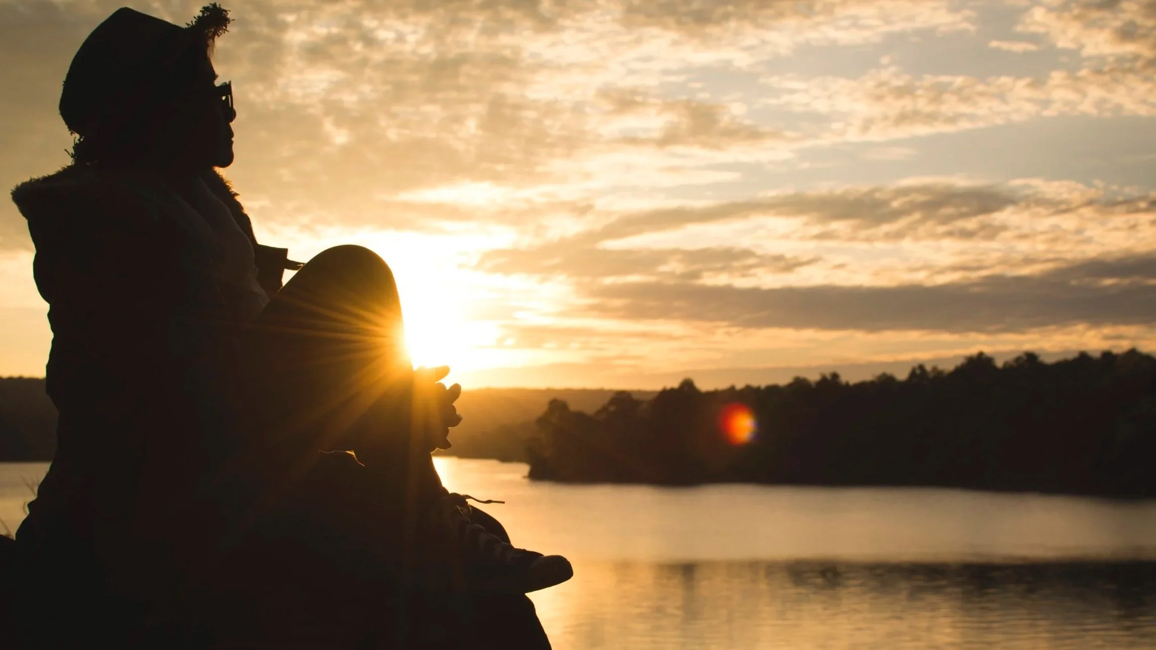 Person sitting at the water’s edge at sunset, symbolizing attentive listening and understanding in consulting.