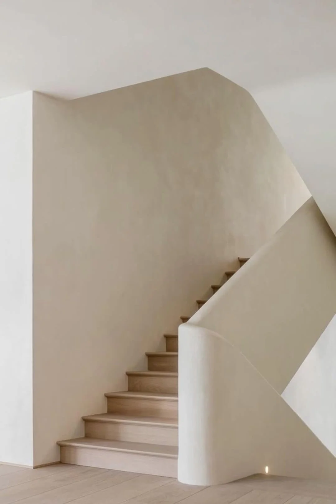 Cream colored microcement custom staircase with seamless curves to complement beautiful white ash floors.