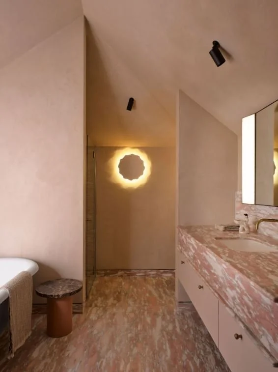 Moody, color drenched microcement bathroom walls and ceiling perfectly complement unique marble floors, vanity and bathtub.