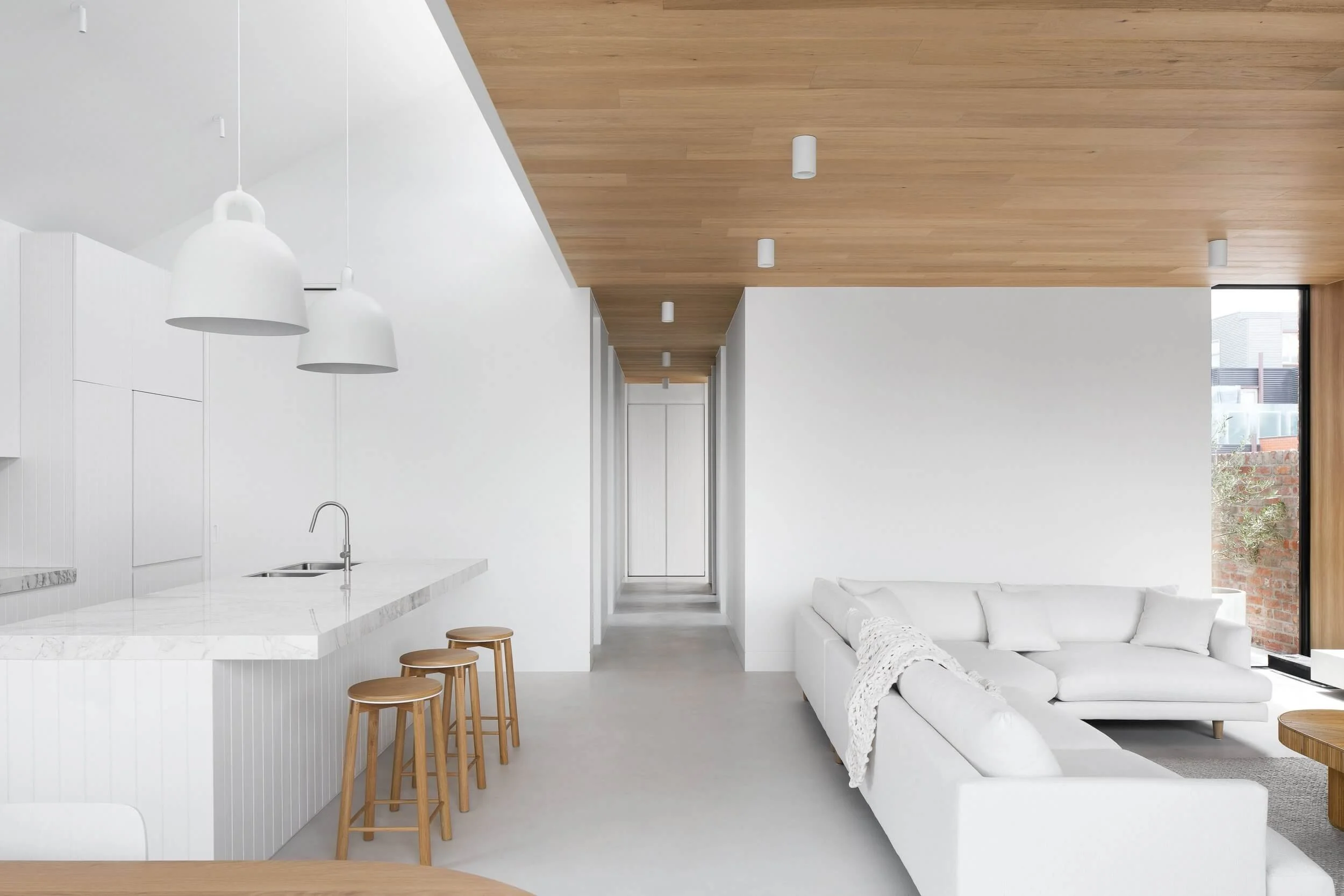 Minimalist living room and kitchen with white walls and wooden ceiling all tied together with seamless light gray microcement floors.