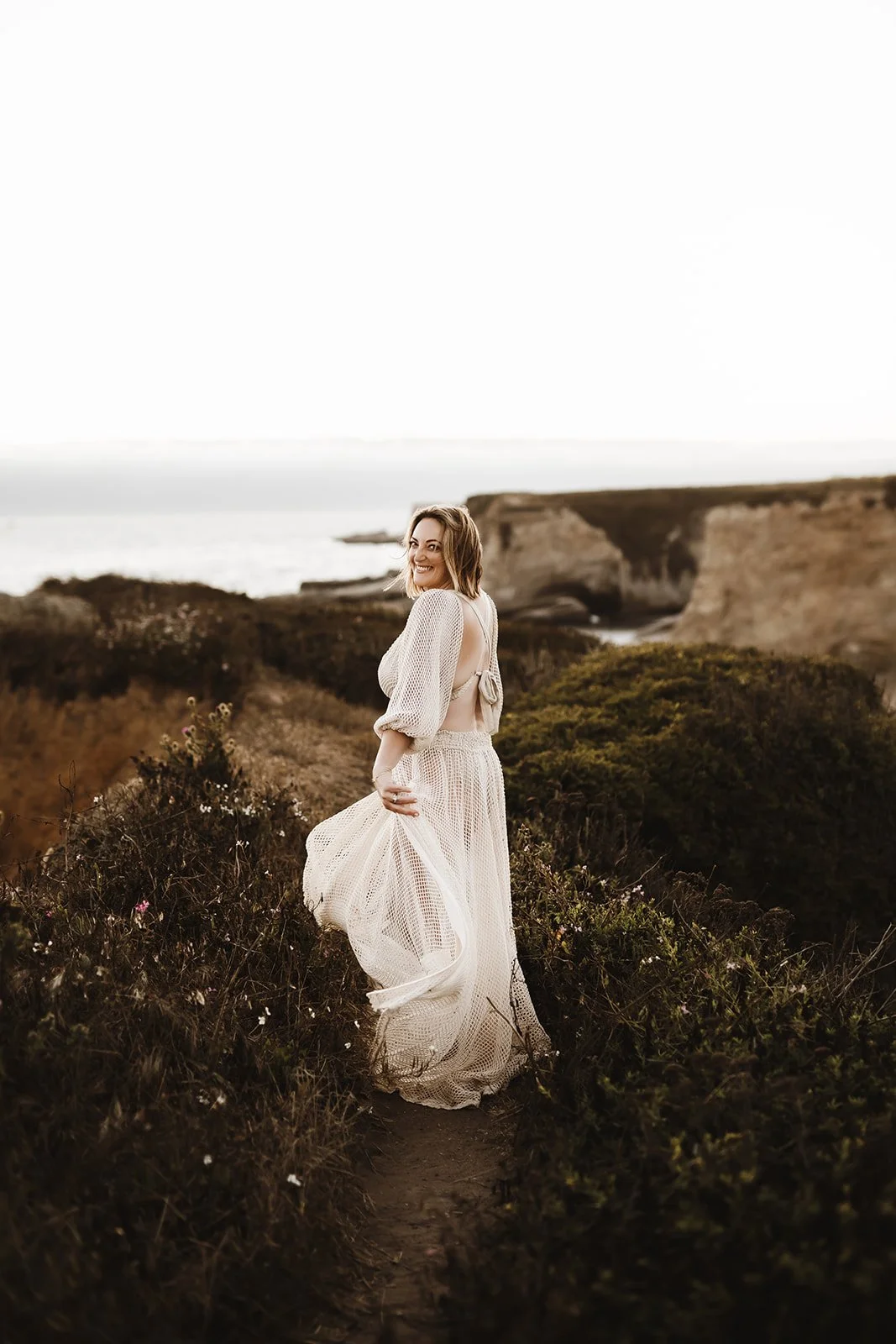 woman smiling in flowy white dress on coastal hillside