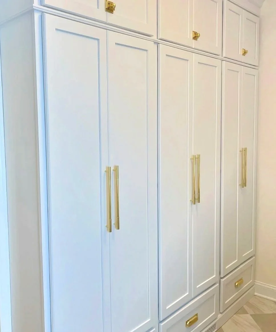 Custom white built-in closet with gold handles in a mudroom with light-colored walls and flooring.