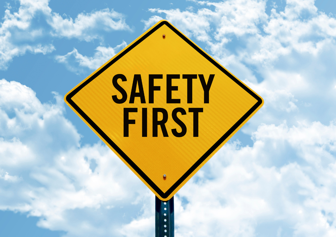 Yellow diamond-shaped safety sign that says 'SAFETY FIRST' against a blue sky with clouds.