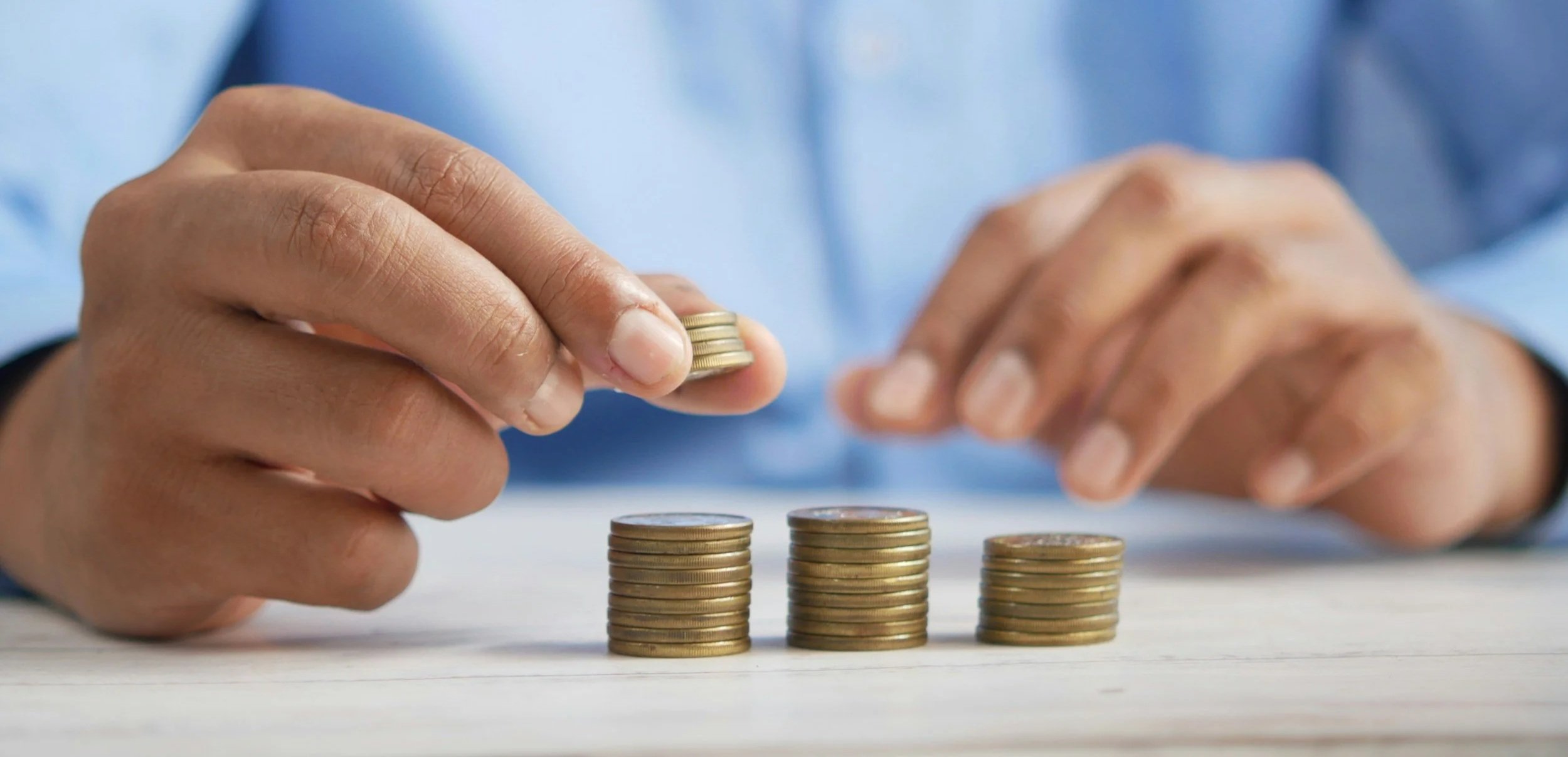 Person stacking coins on a table, with four stacks of coins arranged in increasing order from right to left.