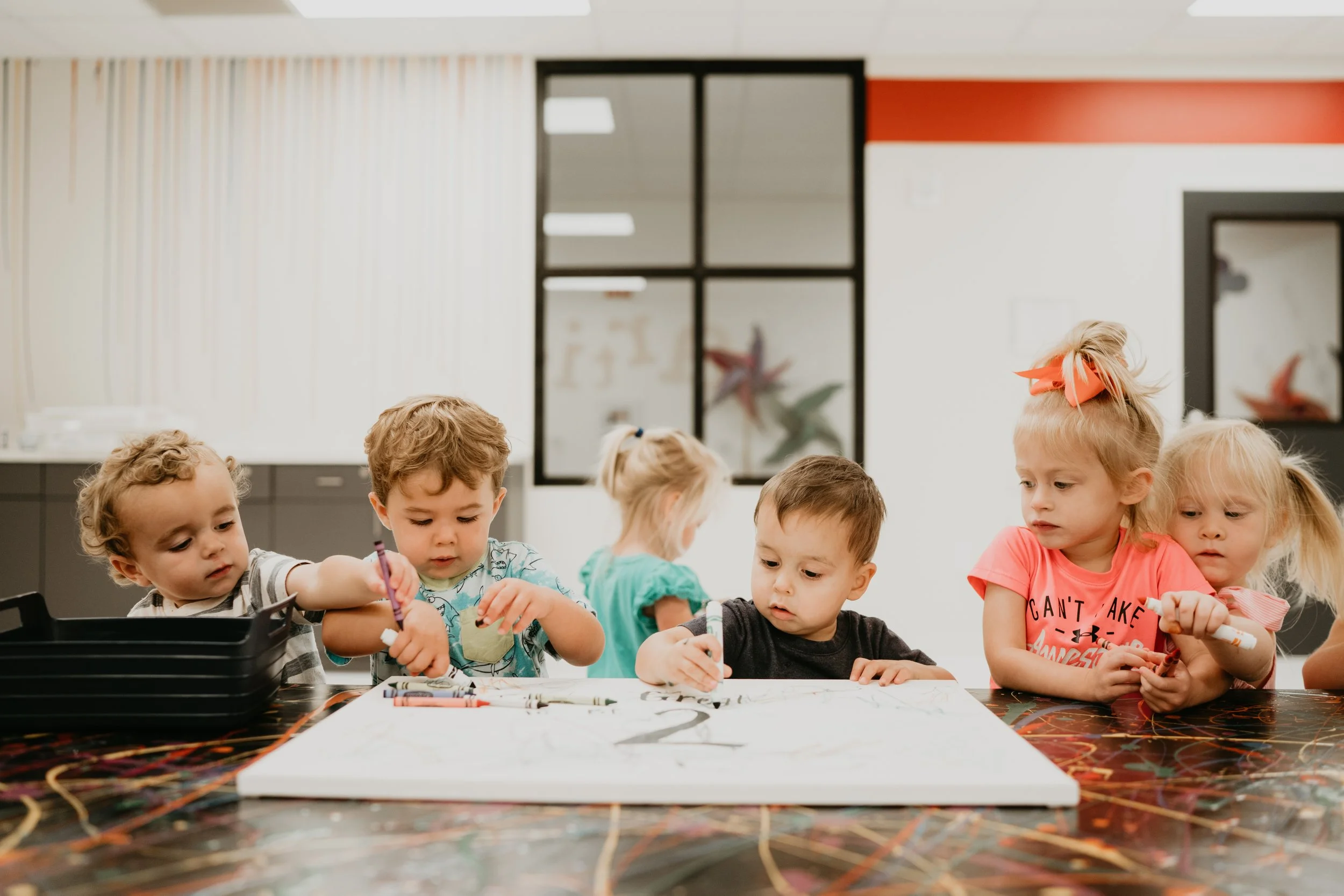 Six young children coloring and drawing at a table in a classroom or art room.