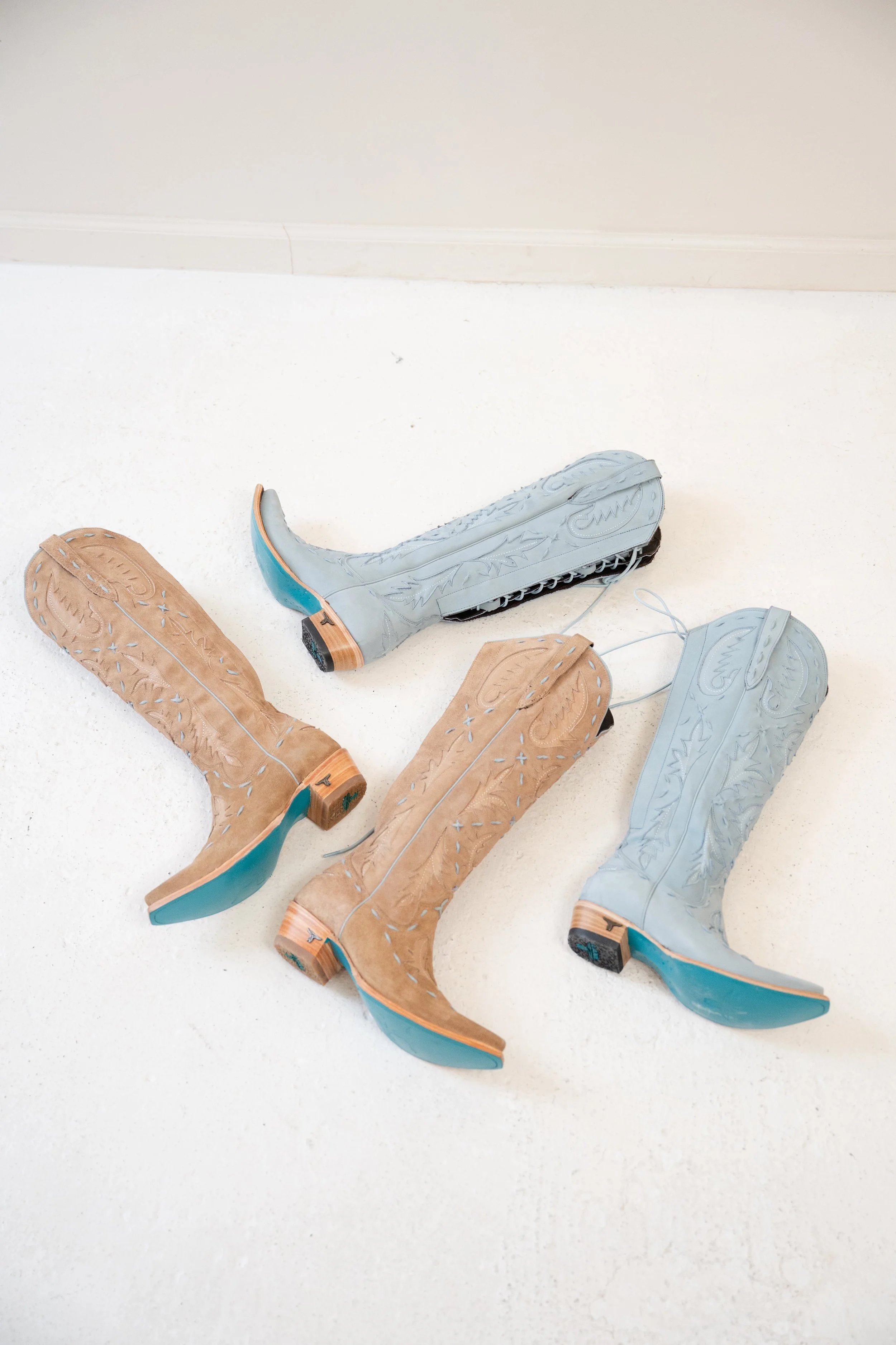 Four cowboy boots, two in tan and two in blue, laid on a white floor.