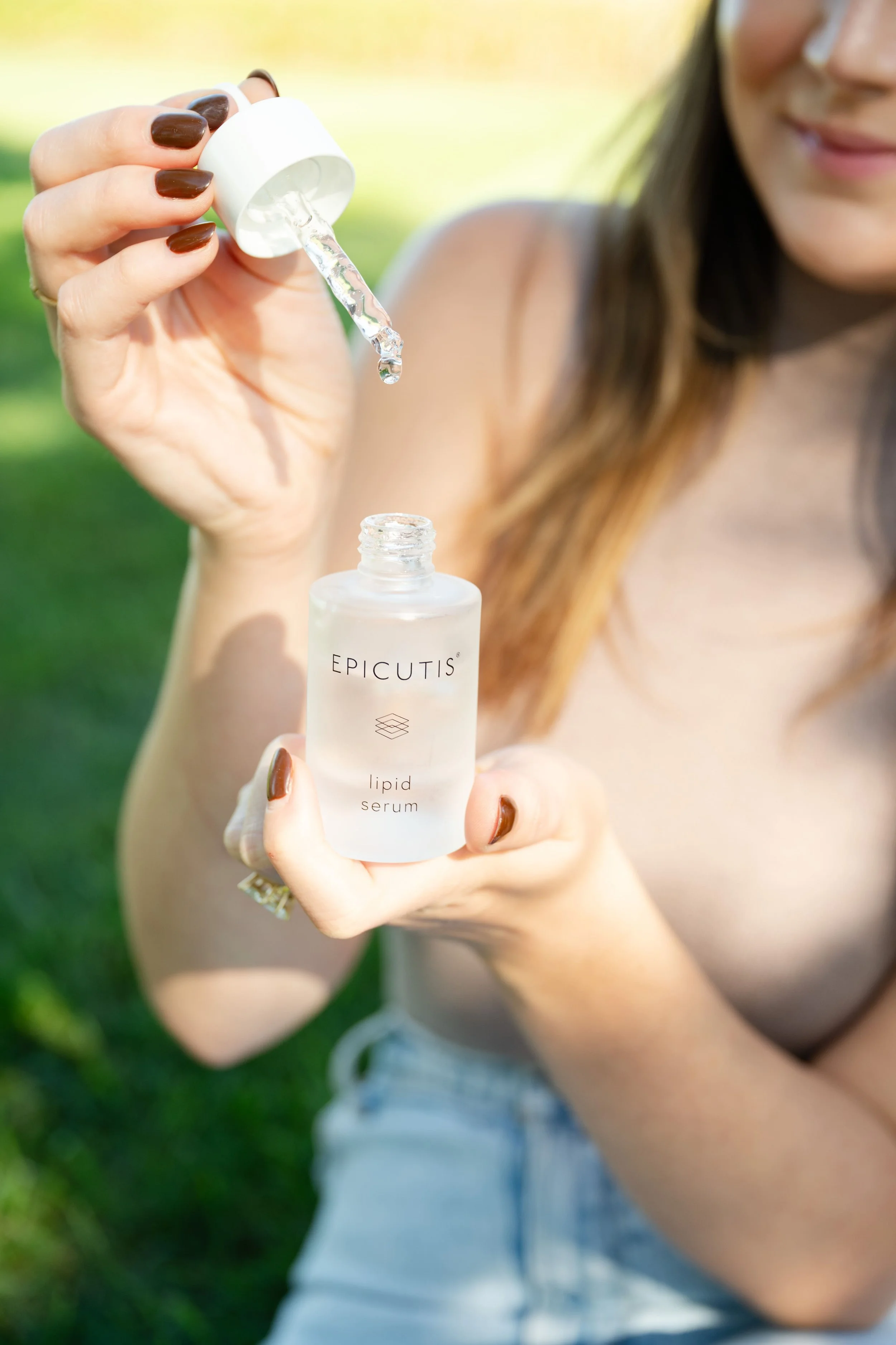 A woman holding a bottle of epicutis lipid serum and pouring some serum from a dropper.