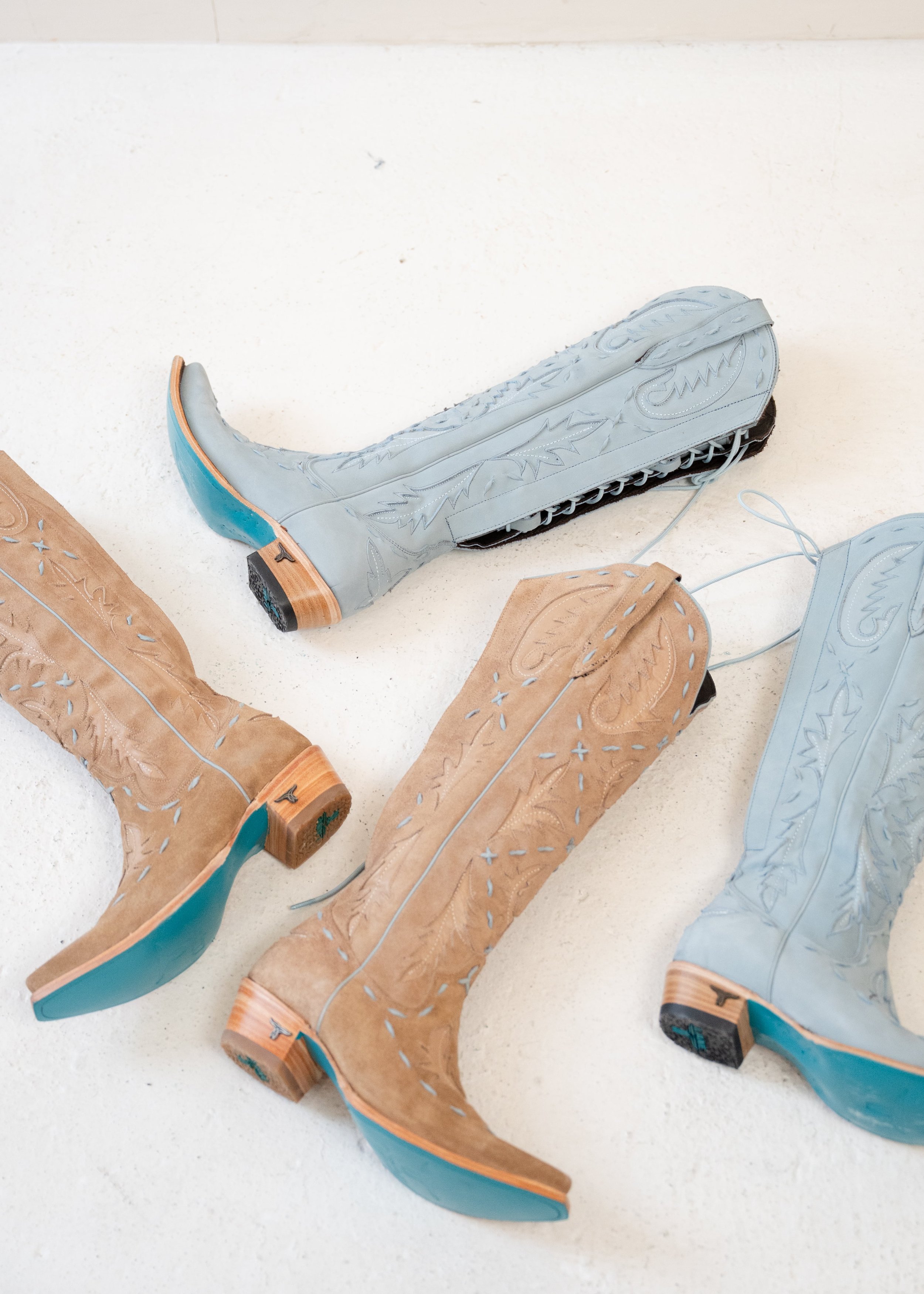 Two pairs of cowboy boots, one in tan and the other in light blue, lying on a white surface.