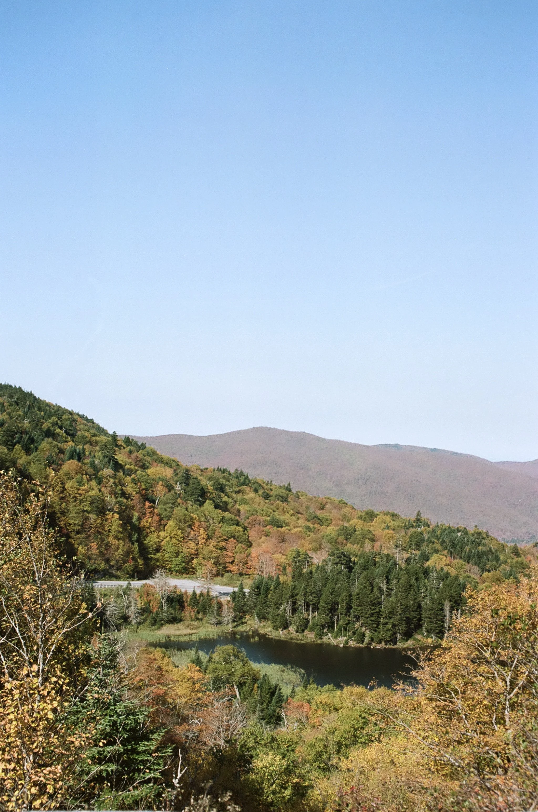Scenic view of a mountain lake surrounded by colorful autumn trees under a clear blue sky.
