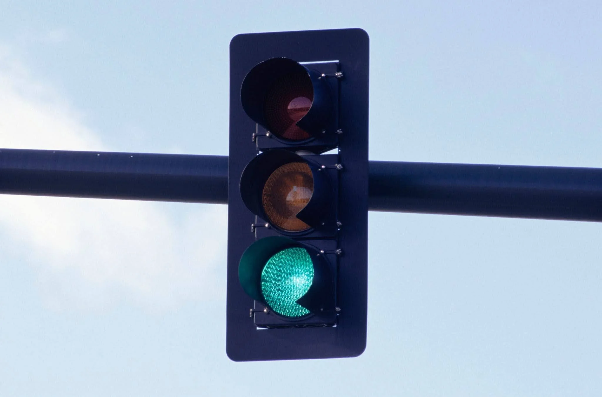 Green traffic light illuminated at an intersection with a clear blue sky in the background.