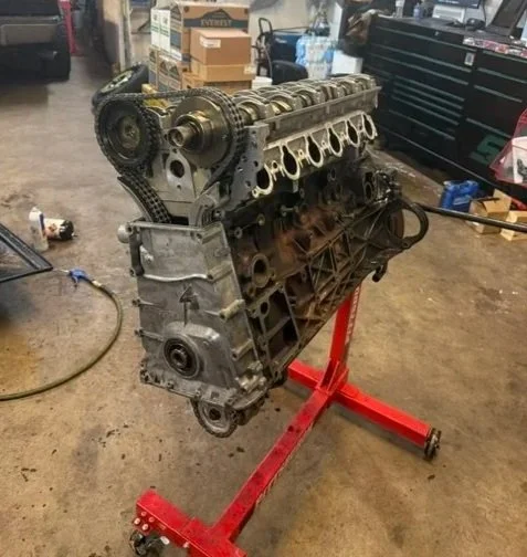 Car engine mounted on a red engine stand in a garage or workshop.