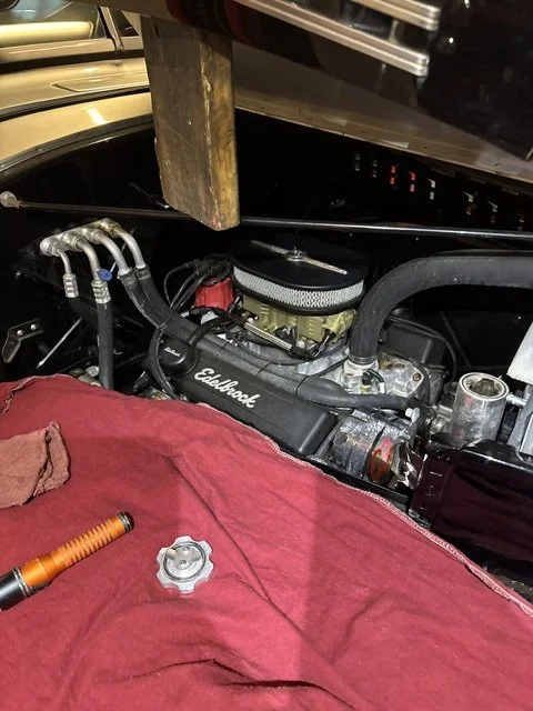 Close-up view of a car engine bay with Edelbrock intake manifold, surrounded by various hoses and tools on a red cloth.