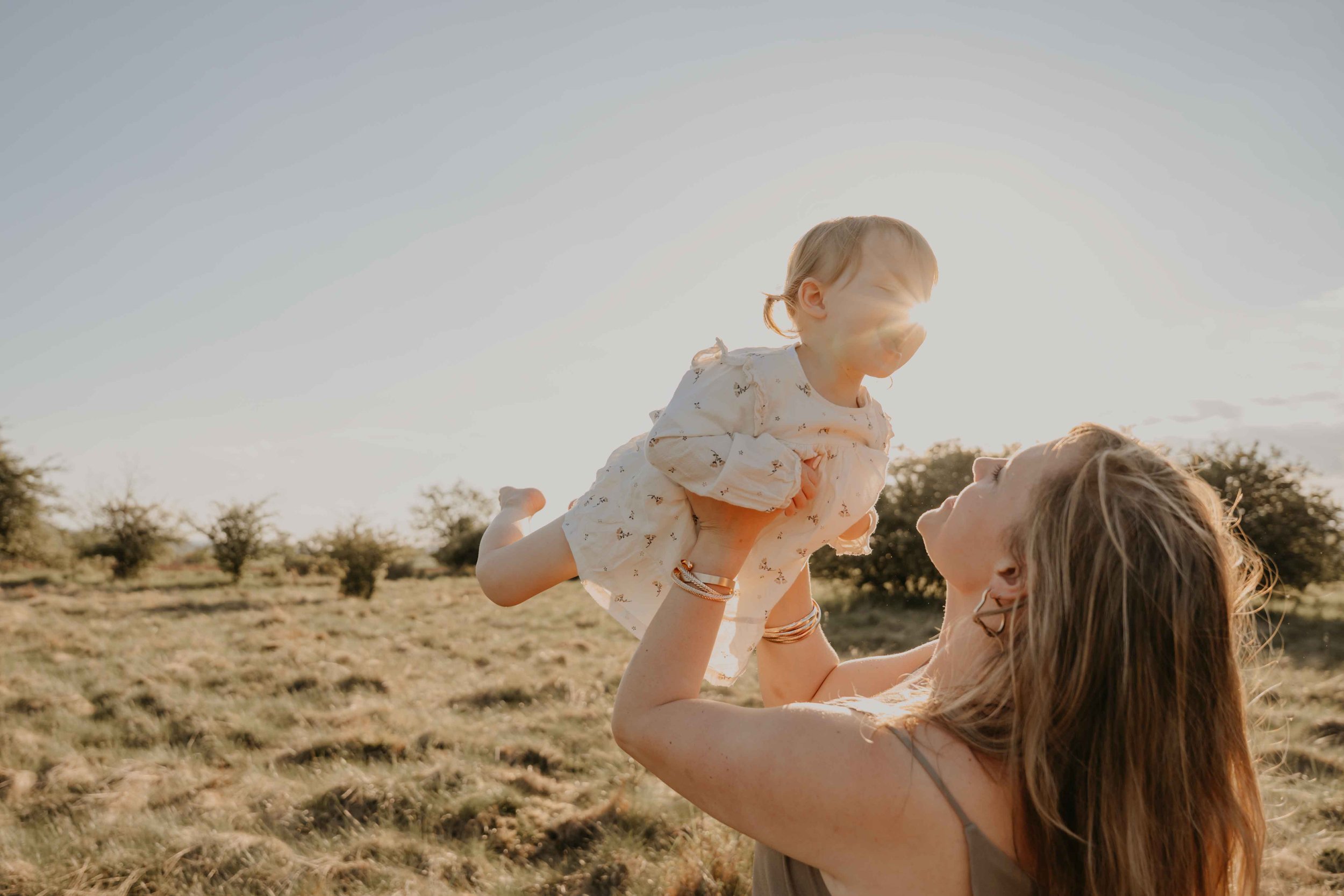 Familienfotografie Nordhessen –Mutter spielt mit ihrer Tochter auf der Wiese im Sonnenuntergang.