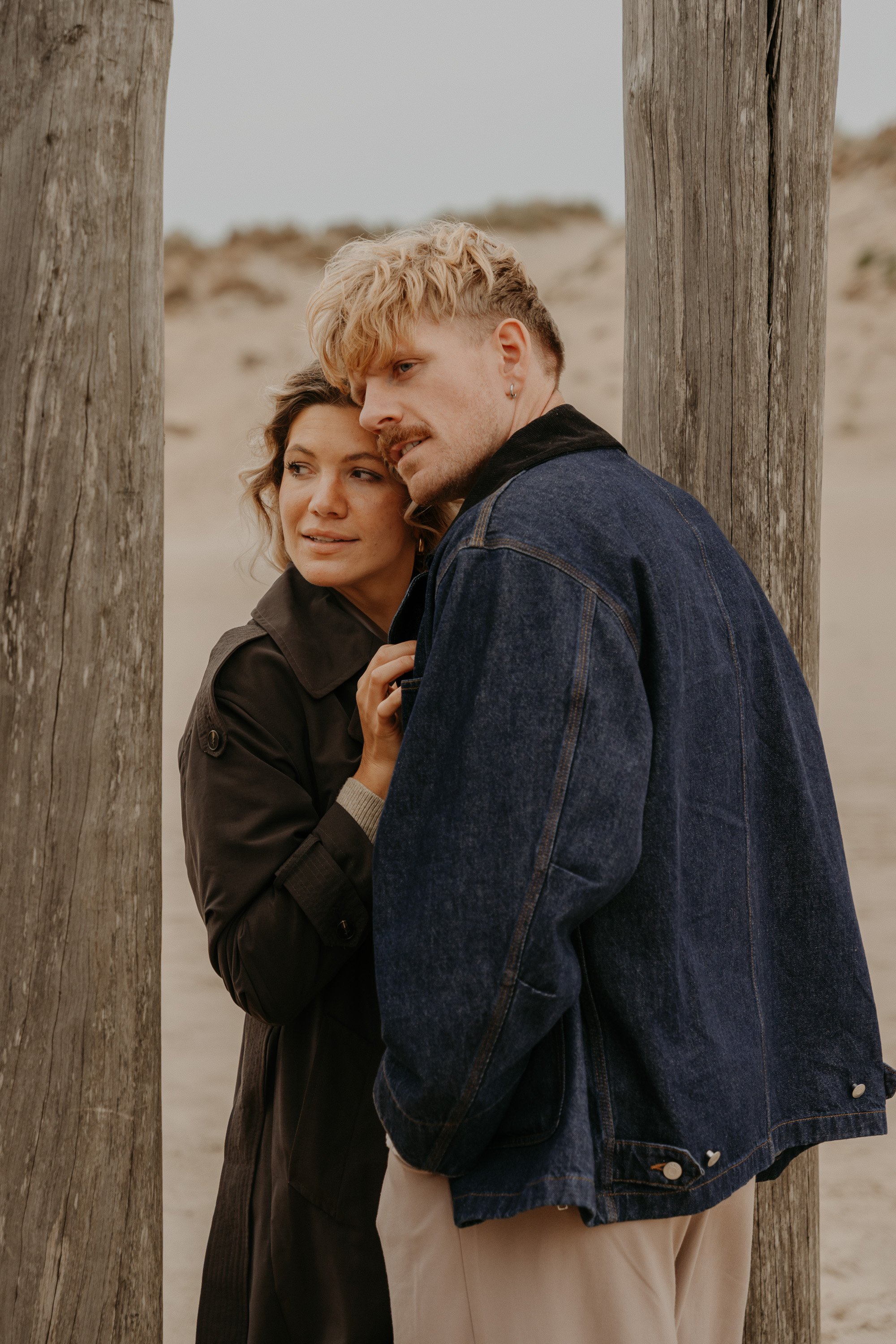 Holländisches Strandshooting – Paar lacht, während Wellen brechen.