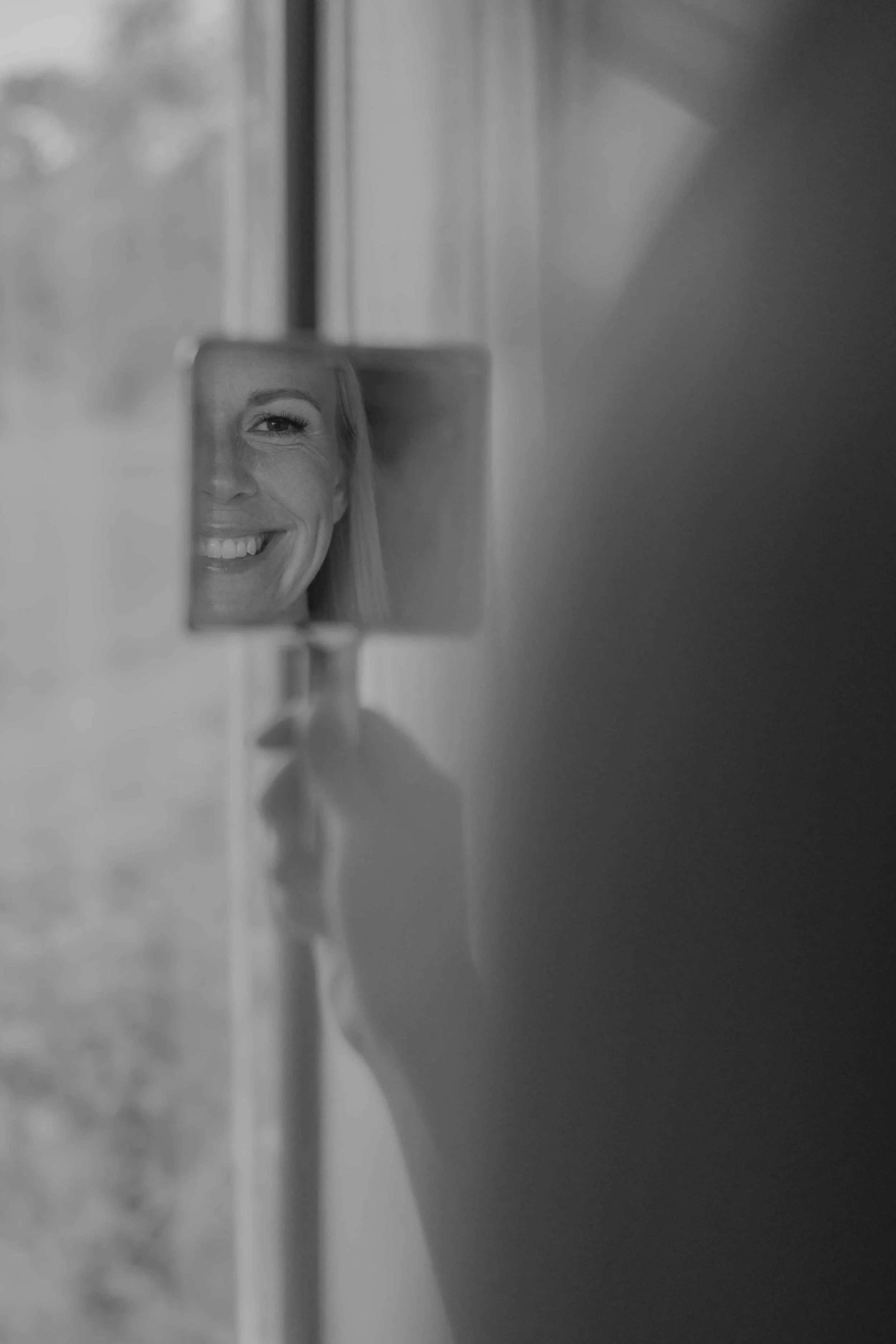 Braut sitzt auf dem Bett in der Suite und schaut sich im Spiegel an. 