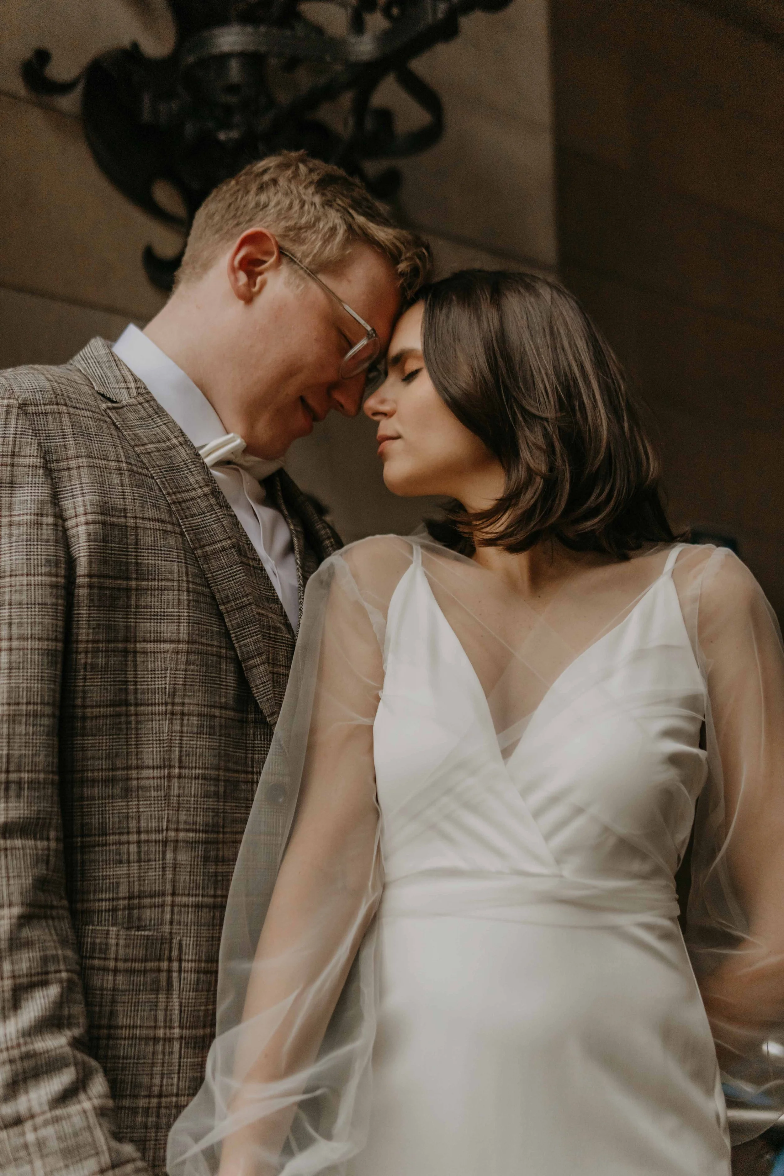 Hochzeitsfotografie Deutschland Norddeutschland – Ein Brautpaar in einer intimen Umarmung, beide mit entspannten und liebevollen Gesichtsausdrücken, die Nase berührend, vor einer dunklen, stilvollen Wand