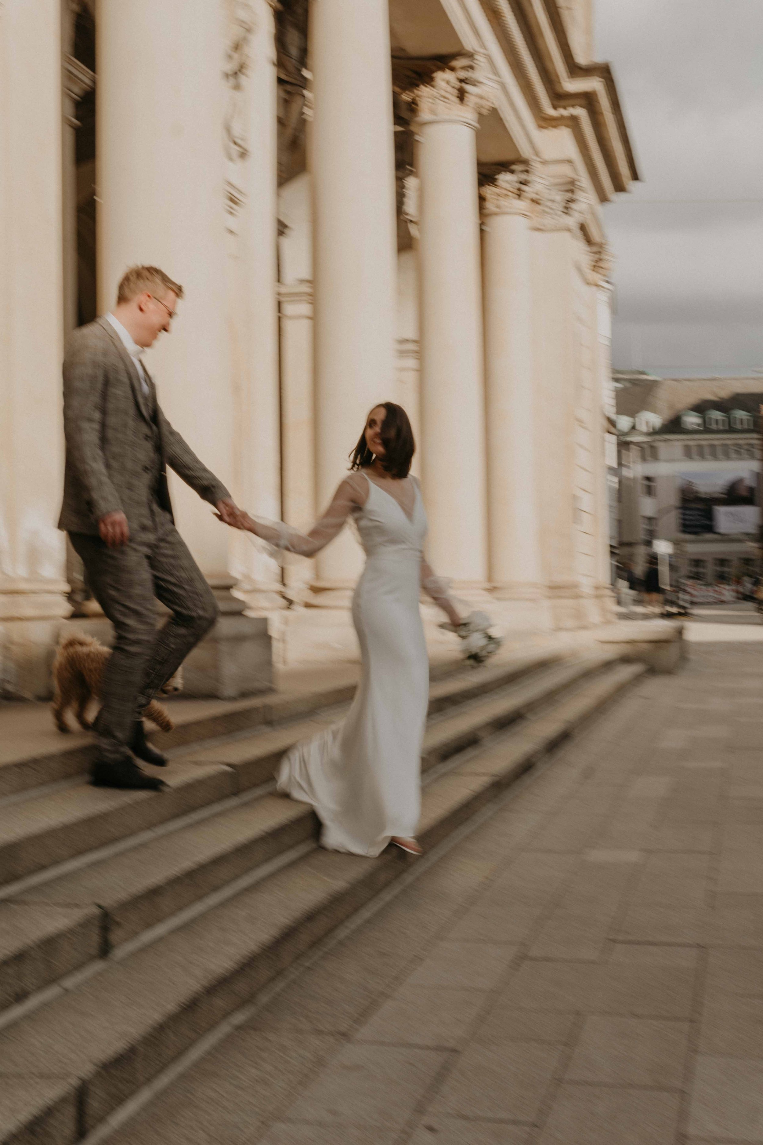 Urbane intime Hochzeit in Hamburger Innenstadt – zarter Moment zwischen Braut und Bräutigam, sie laufen Händchen haltend durch die alten Gebäude der Innenstadt, Handelskammer. Das Bild hat Bewegungsunschärfe.