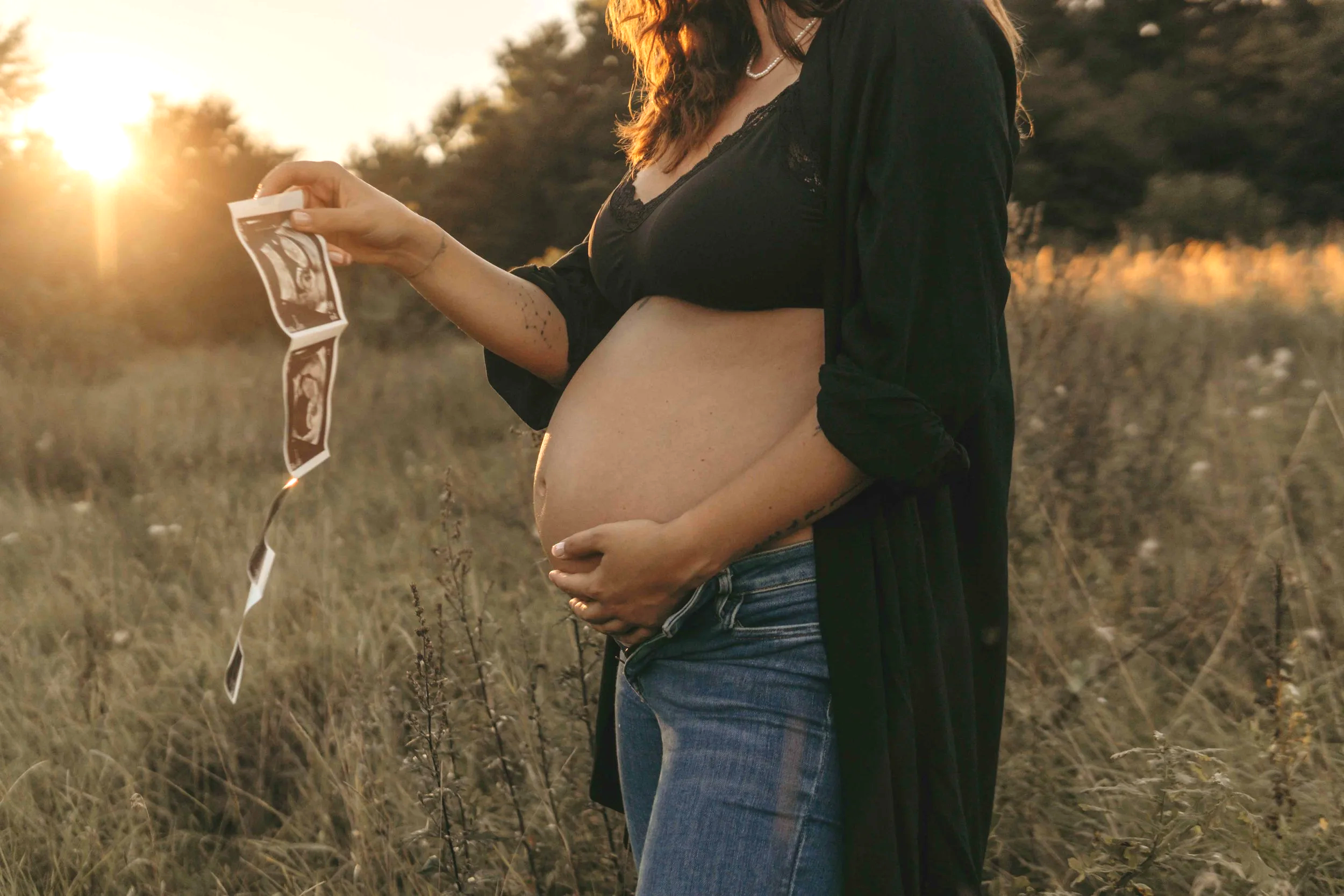 Babybauchshooting Hamburg – werdende Mutter hält zärtlich ihren Bauch im Sonnenuntergang.