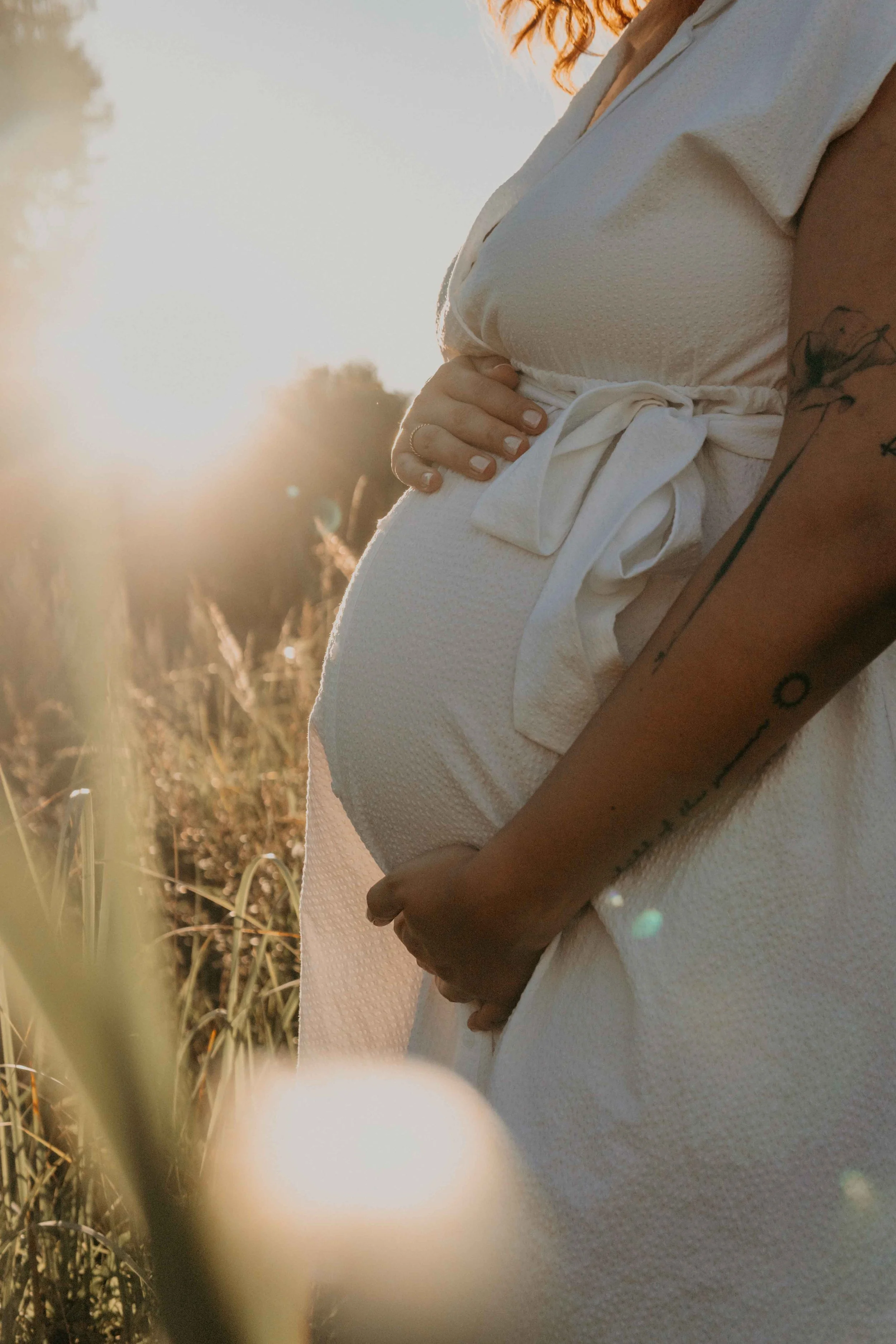 Babybauchshooting Hamburg – werdende Mutter hält zärtlich ihren Bauch im Sonnenuntergang.