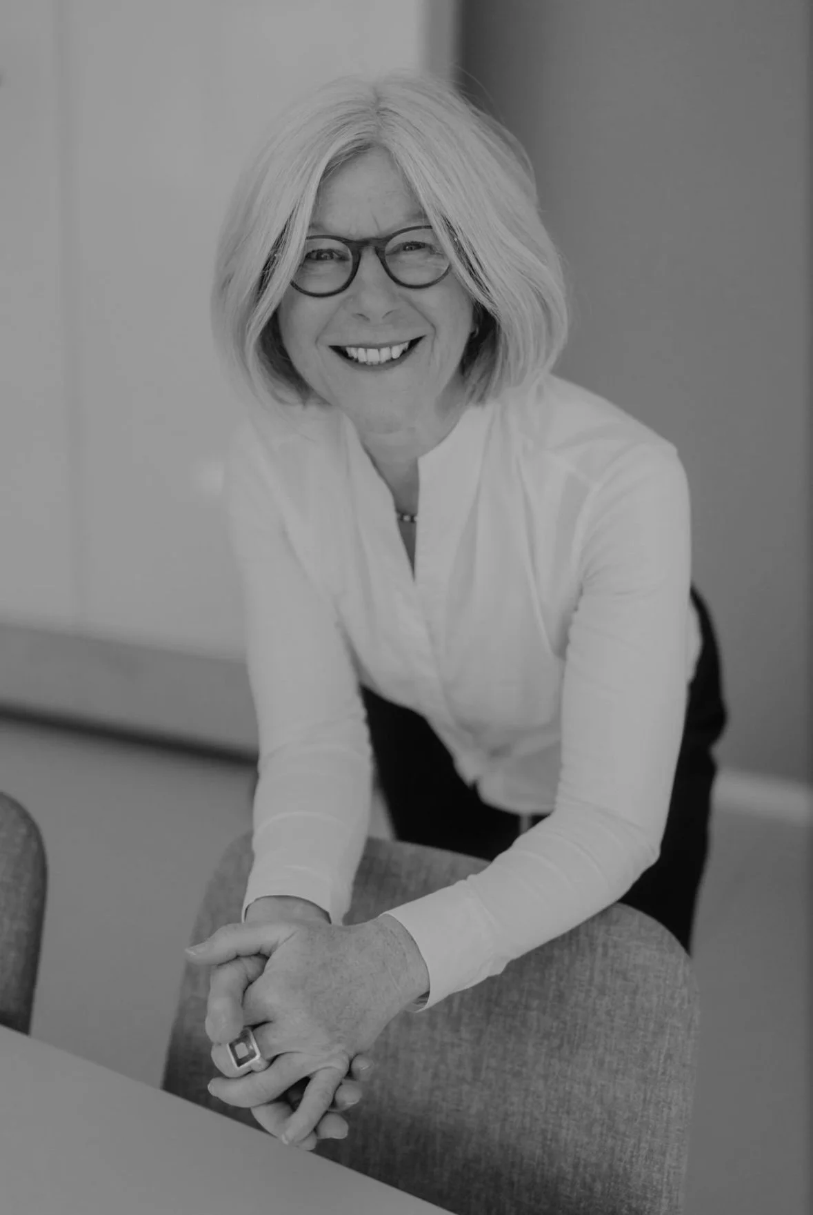 Business Porträt Shooting mit Britta Trompeter, Business Coach. Frau lächelt natürlich in die Kamera und lehnt auf Stuhl.