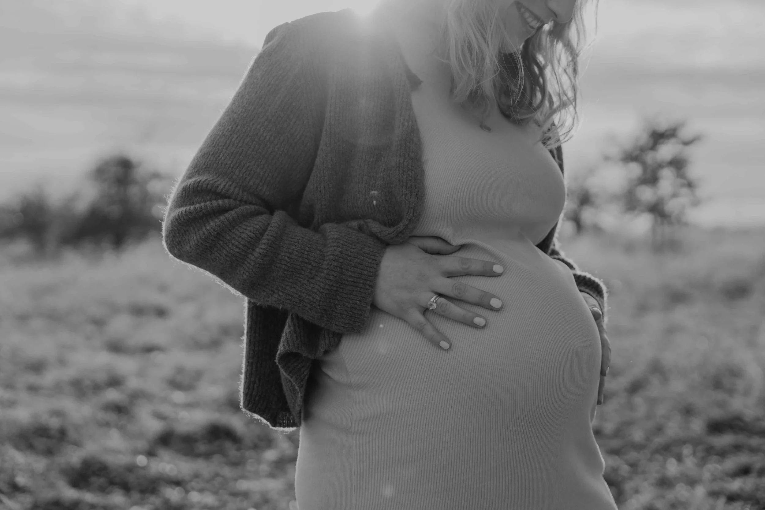Schwangerschaftsfotografie Kassel – Mutter sitzt im Gras, Sonnenstrahlen auf Babybauch.