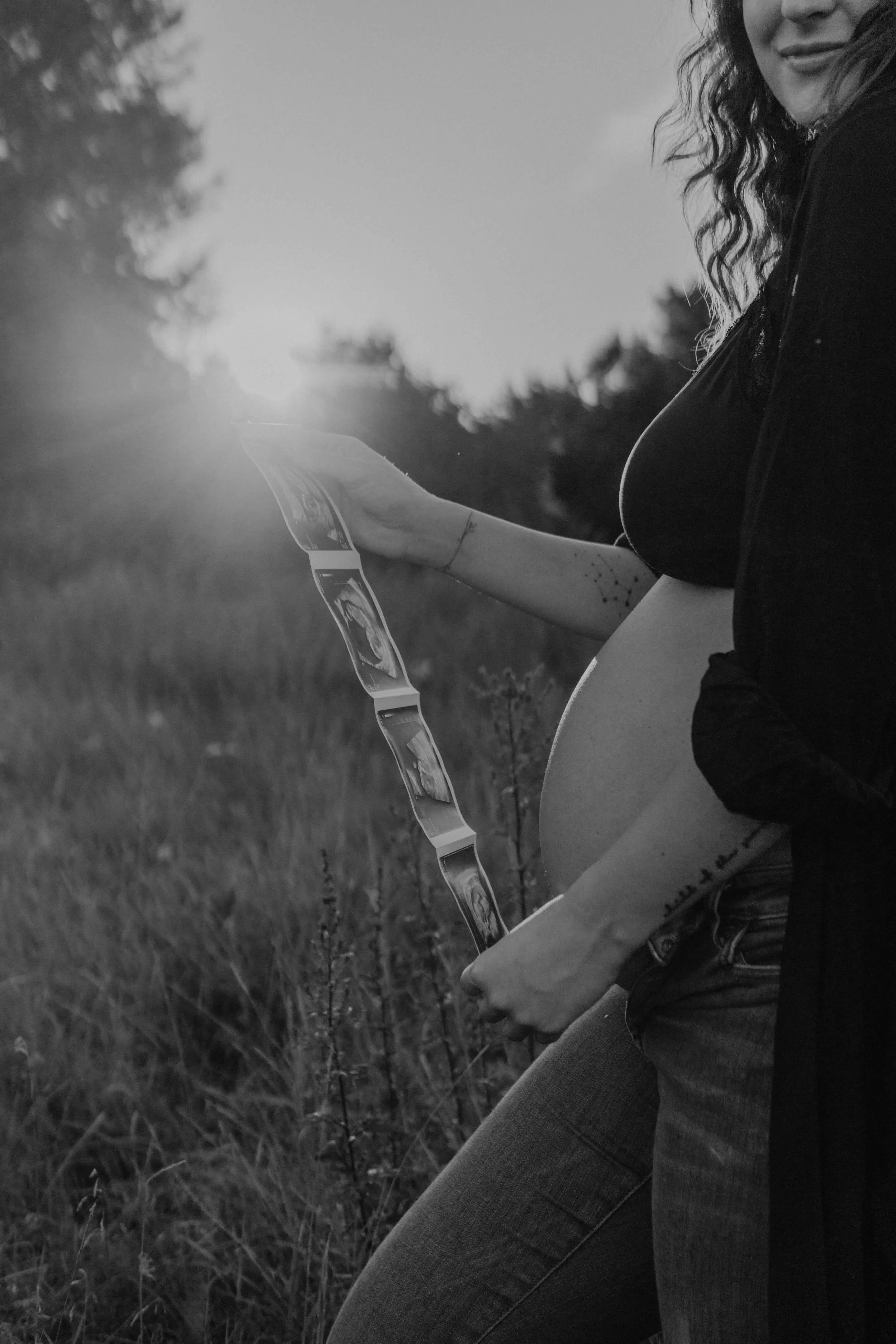 Babybauchshooting Hamburg – werdende Mutter hält zärtlich ihren Bauch und das Ultraschallbild im Sonnenuntergang.