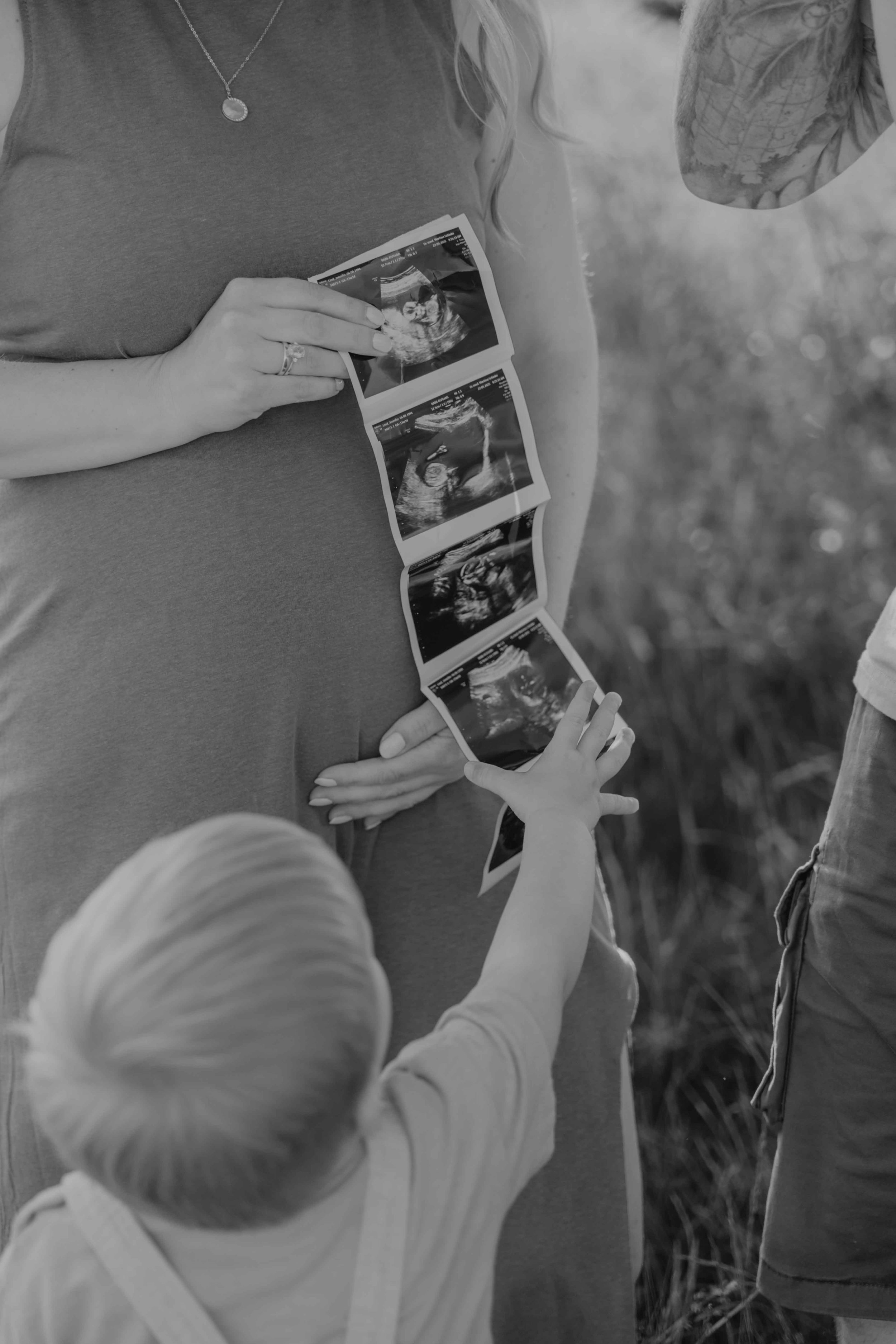 Babybauchshooting Nordhessen – werdende Mutter hält Ultraschall, Sohn greift danach.