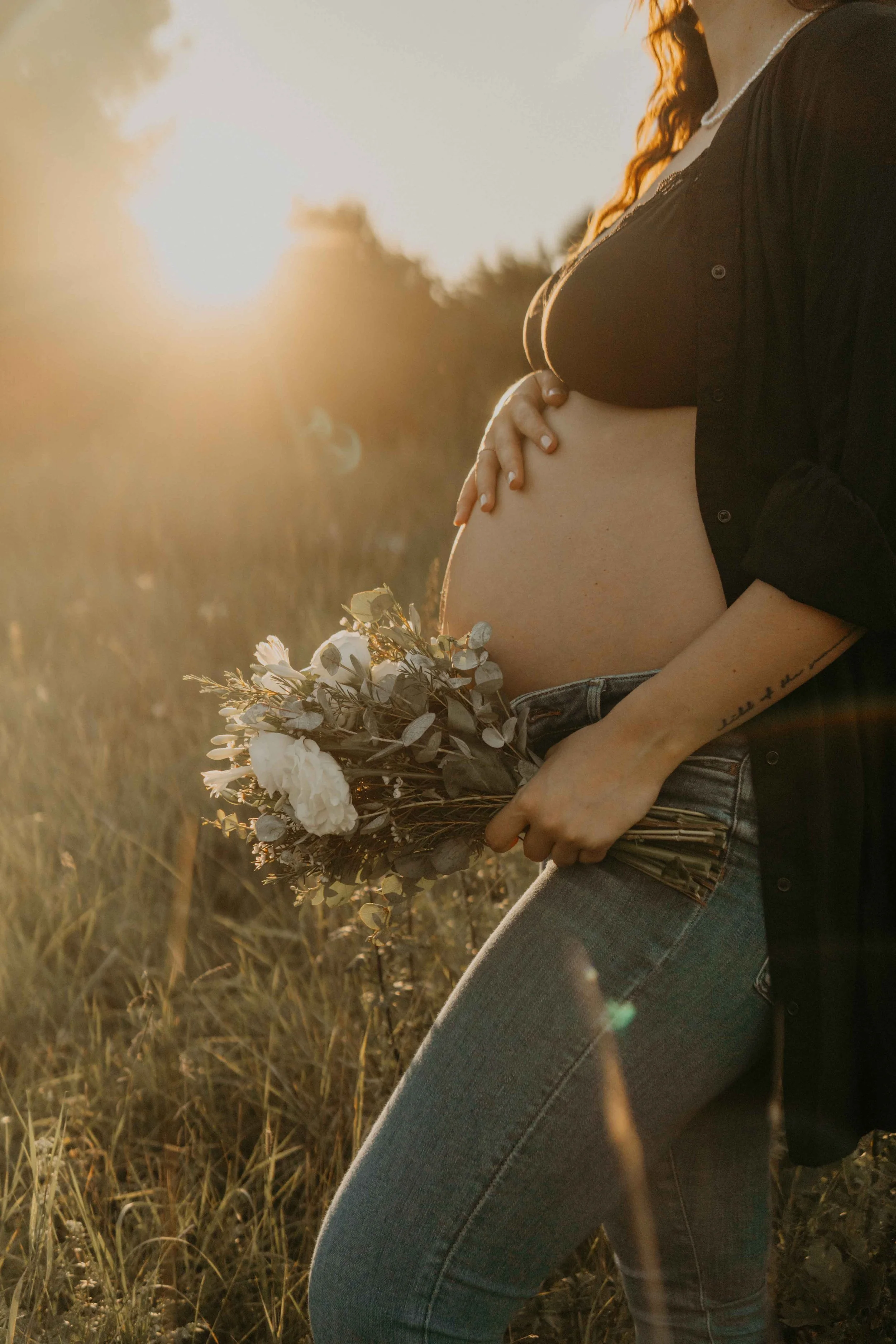 Babybauchshooting Hamburg – werdende Mutter hält zärtlich ihren Bauch im Sonnenuntergang.