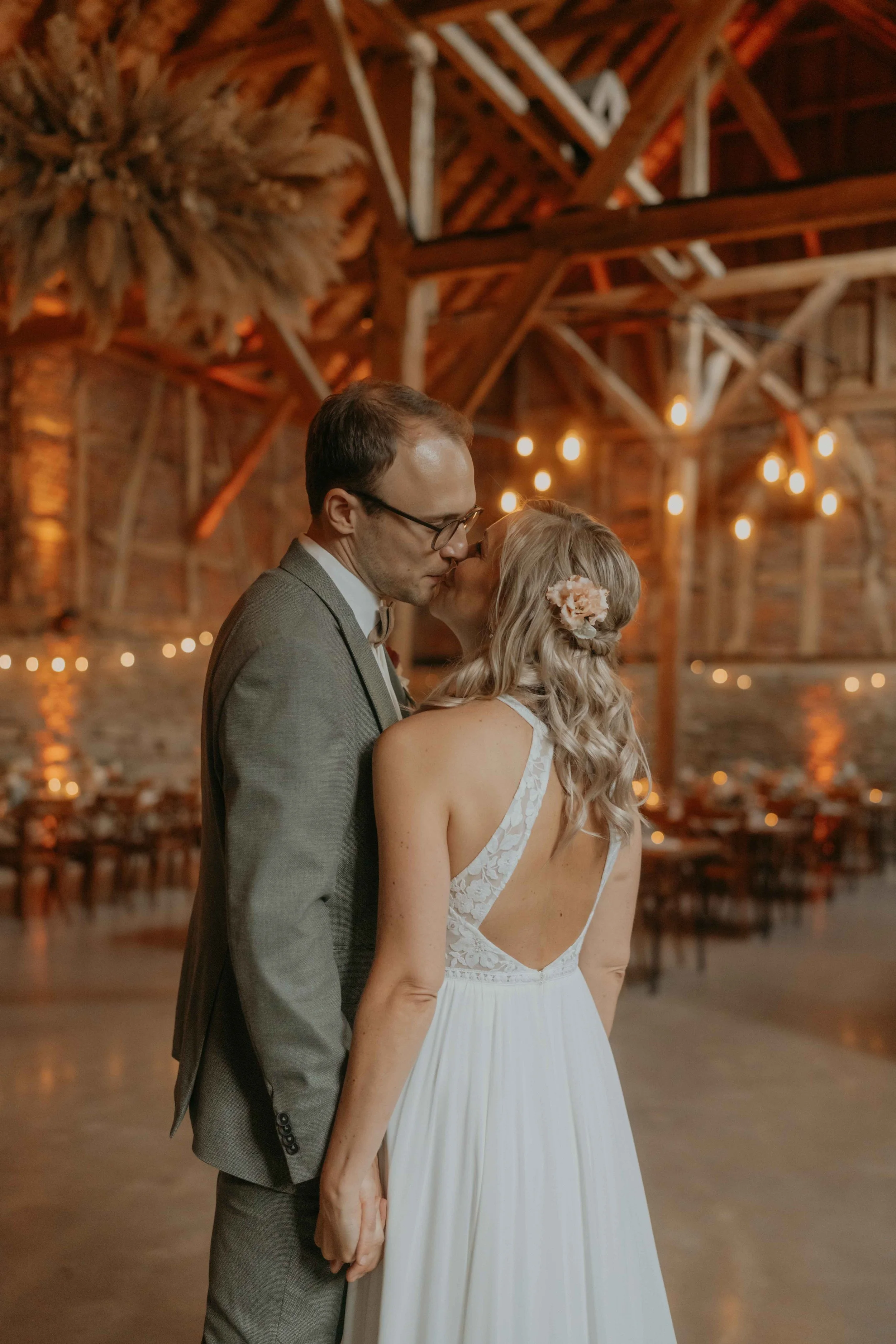Lichterketten an der Scheunendecke, gemütliche Stimmung im Festsaal und Brautpaar küssend in der Mitte des Saals.
