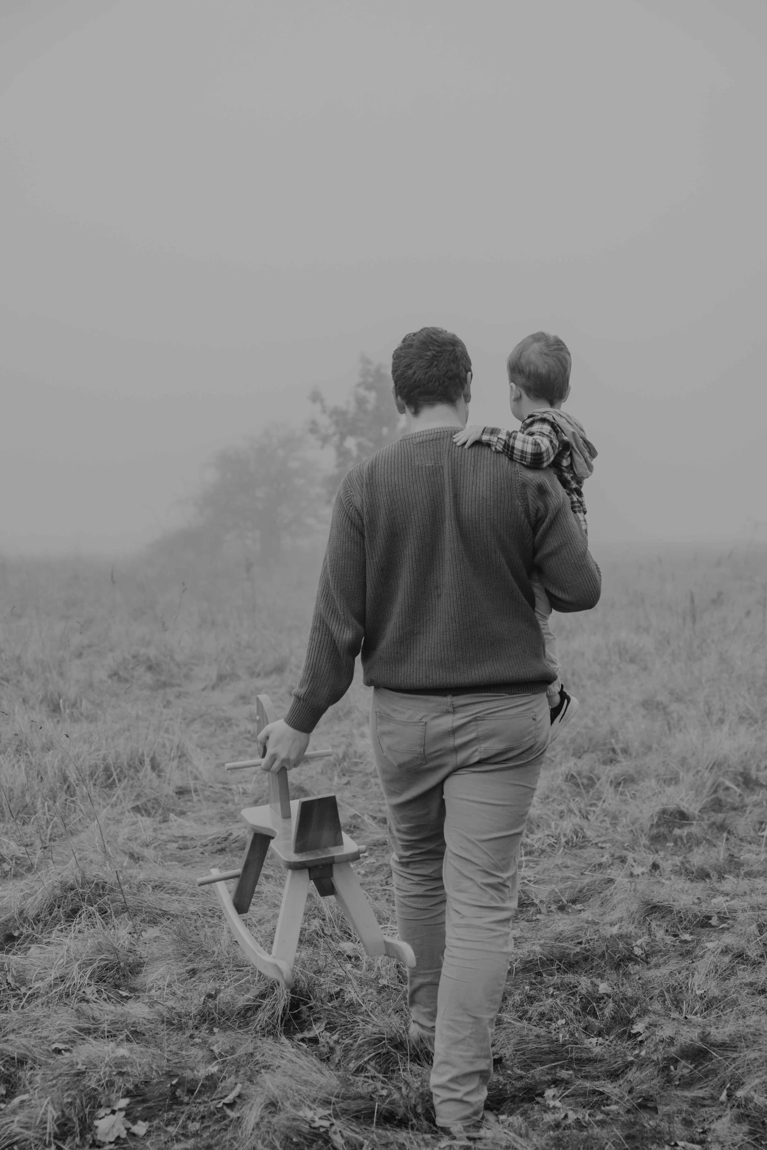 Familienfotograf Nordhessen – Vater trägt Sohn auf dem Arm, Schaukelpferd in der Hand tragend.