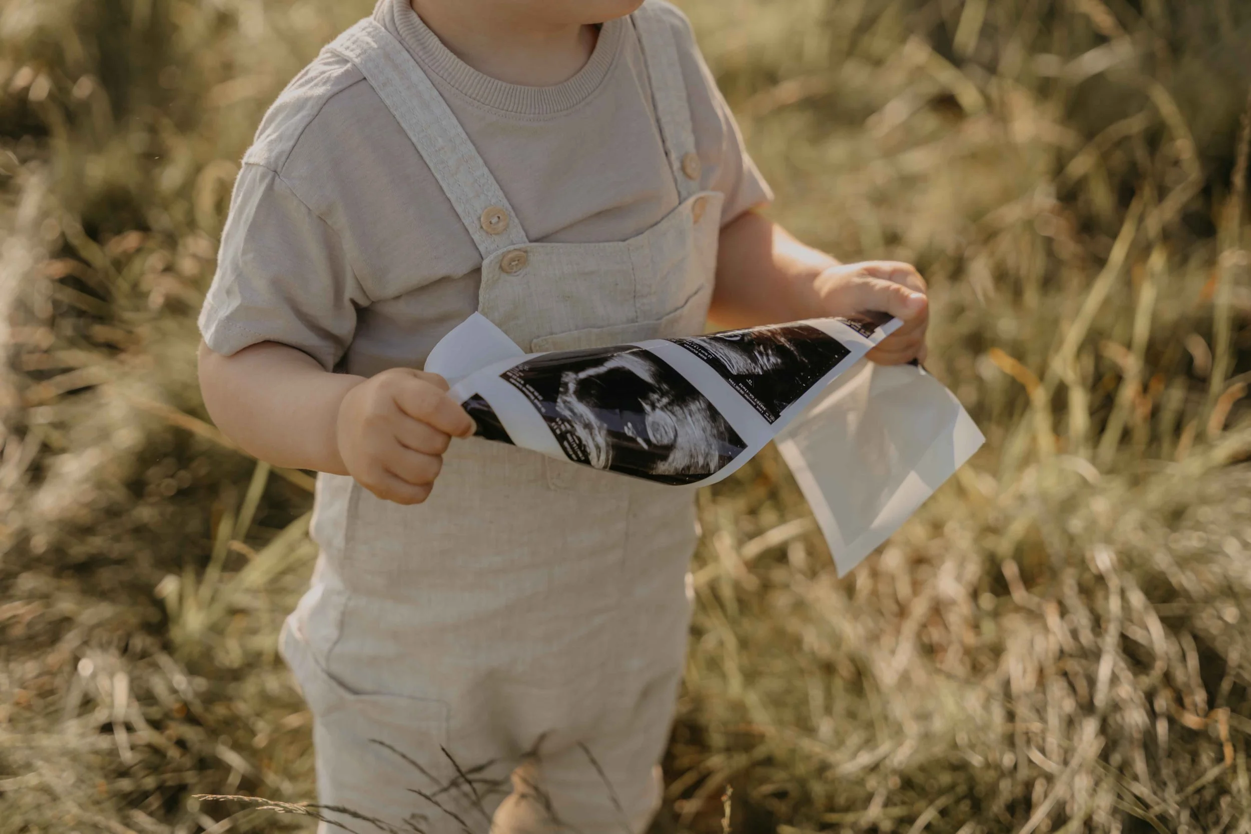 Familienshooting draußen – Kinder laufen barfuß über eine Wiese, hält Ultraschall in den Händen.