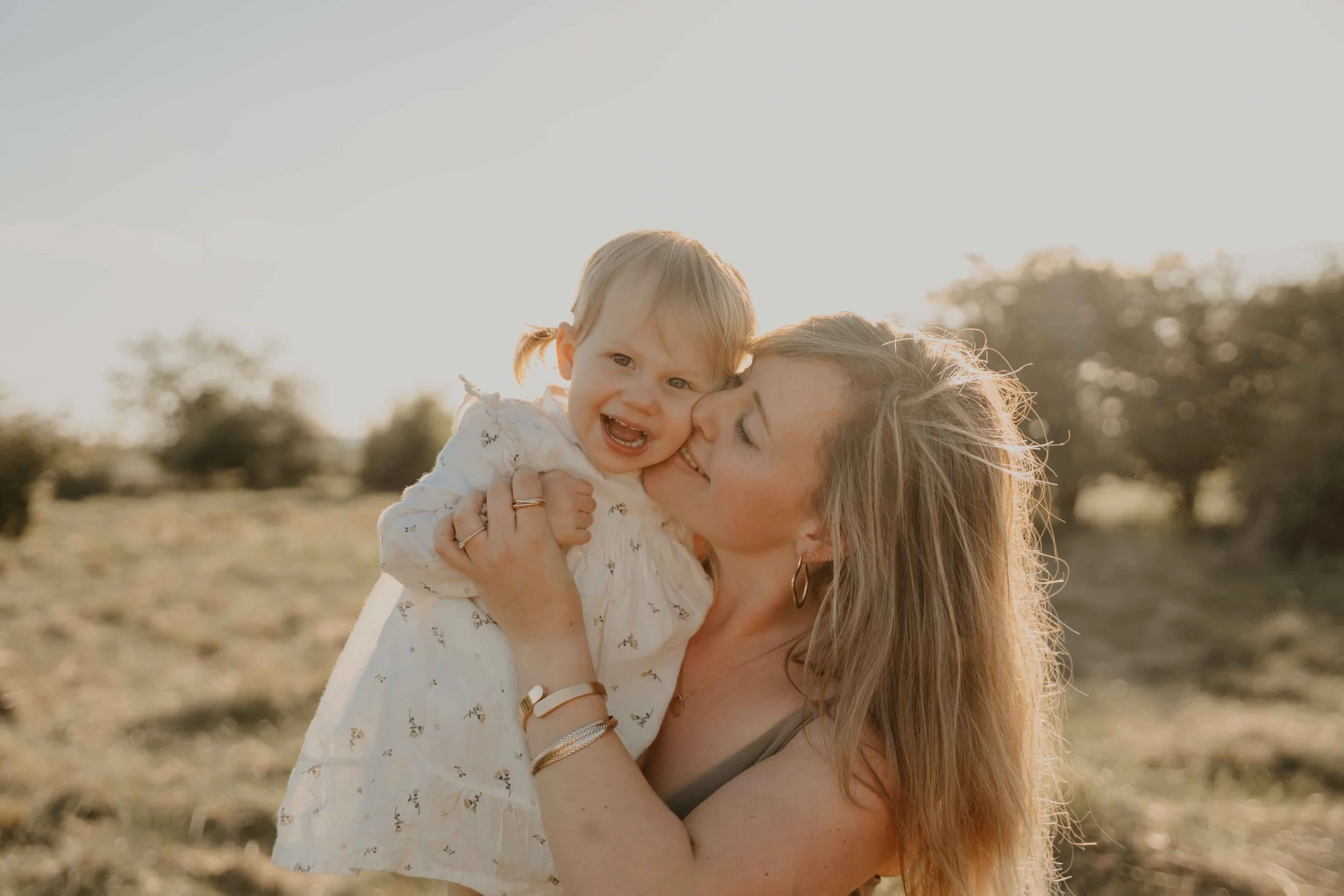 Familienfotografie Nordhessen –Mutter hält Tochter lieb auf der Wiese im Sonnenuntergang.
