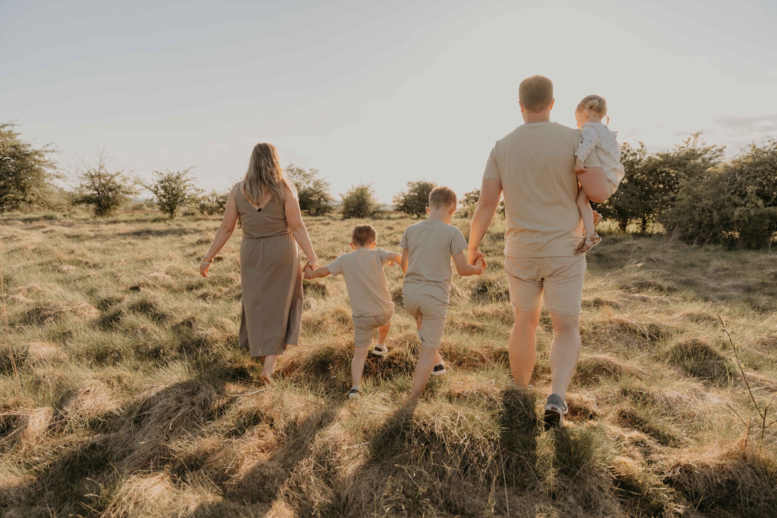 Familienfotografie Korbach –Familie geht Hand in Hand im Sonnenuntergang spazieren.