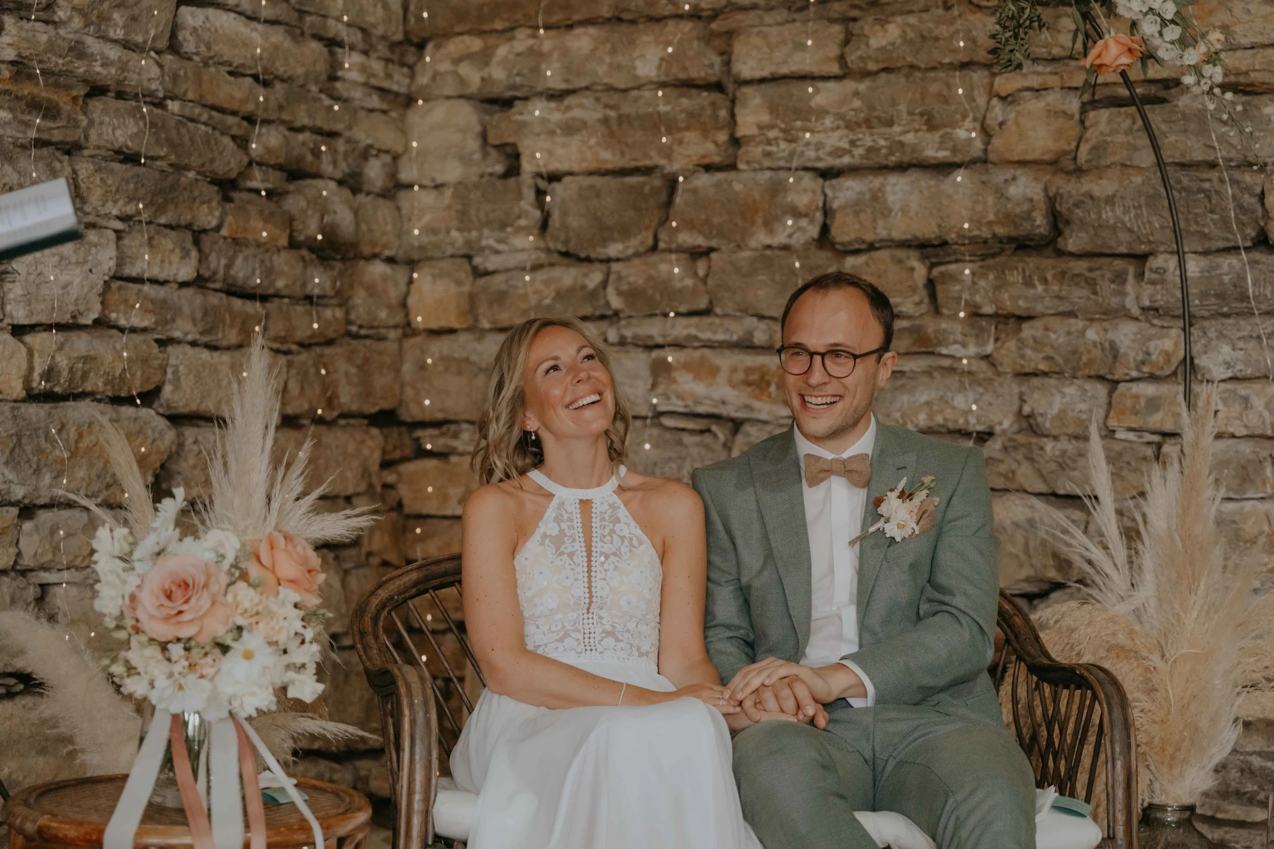 Freie Trauung Nordhessen – Braut und Bräutigam sitzen in der Scheune, aus tiefem Herzen lachend, vor ihren Gästen.