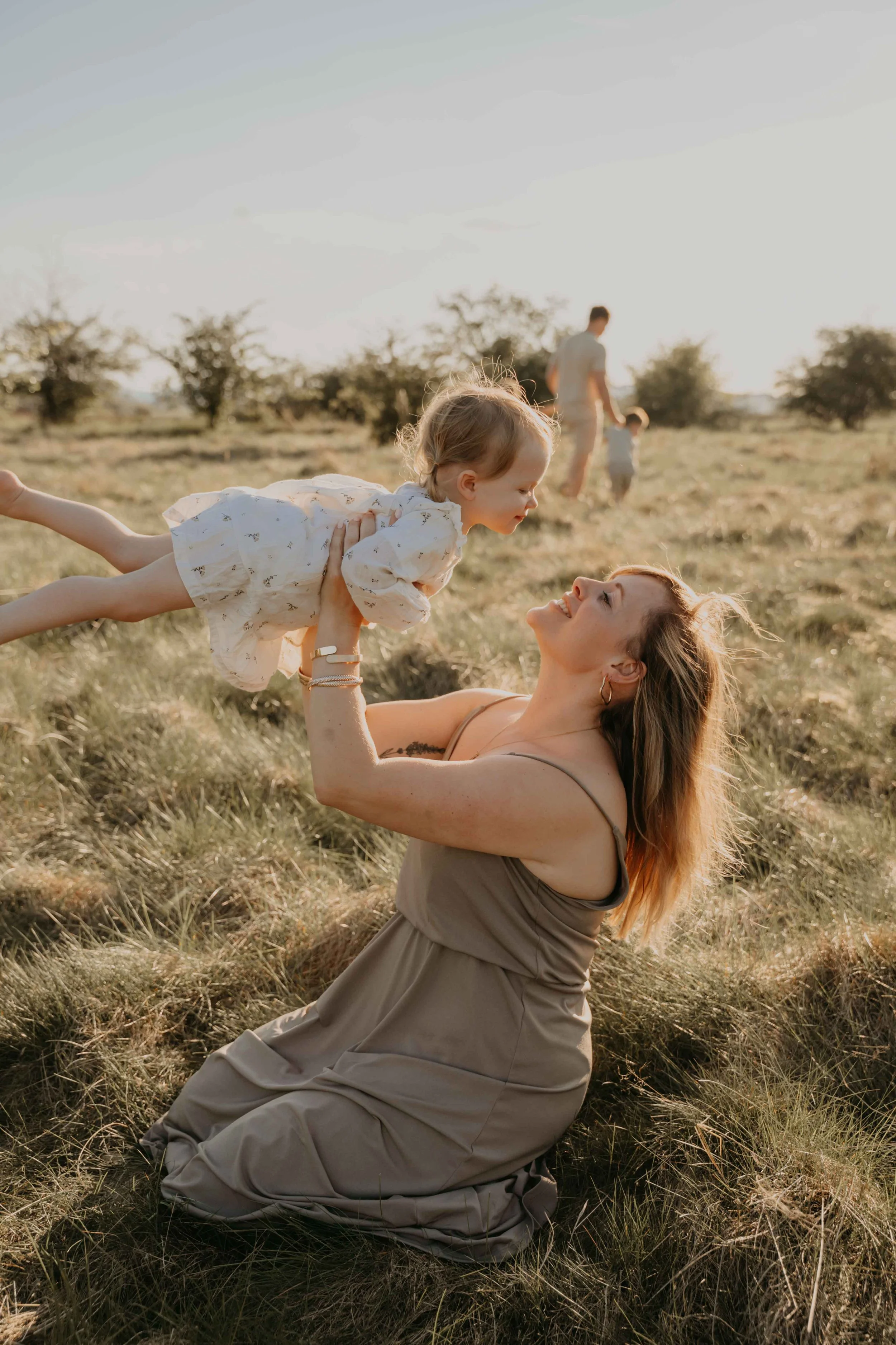 Familienfotografie Nordhessen –Mutter wirft ihre Tochter spielend in die Luft. Vater geht mit Geschwistern spazieren. 