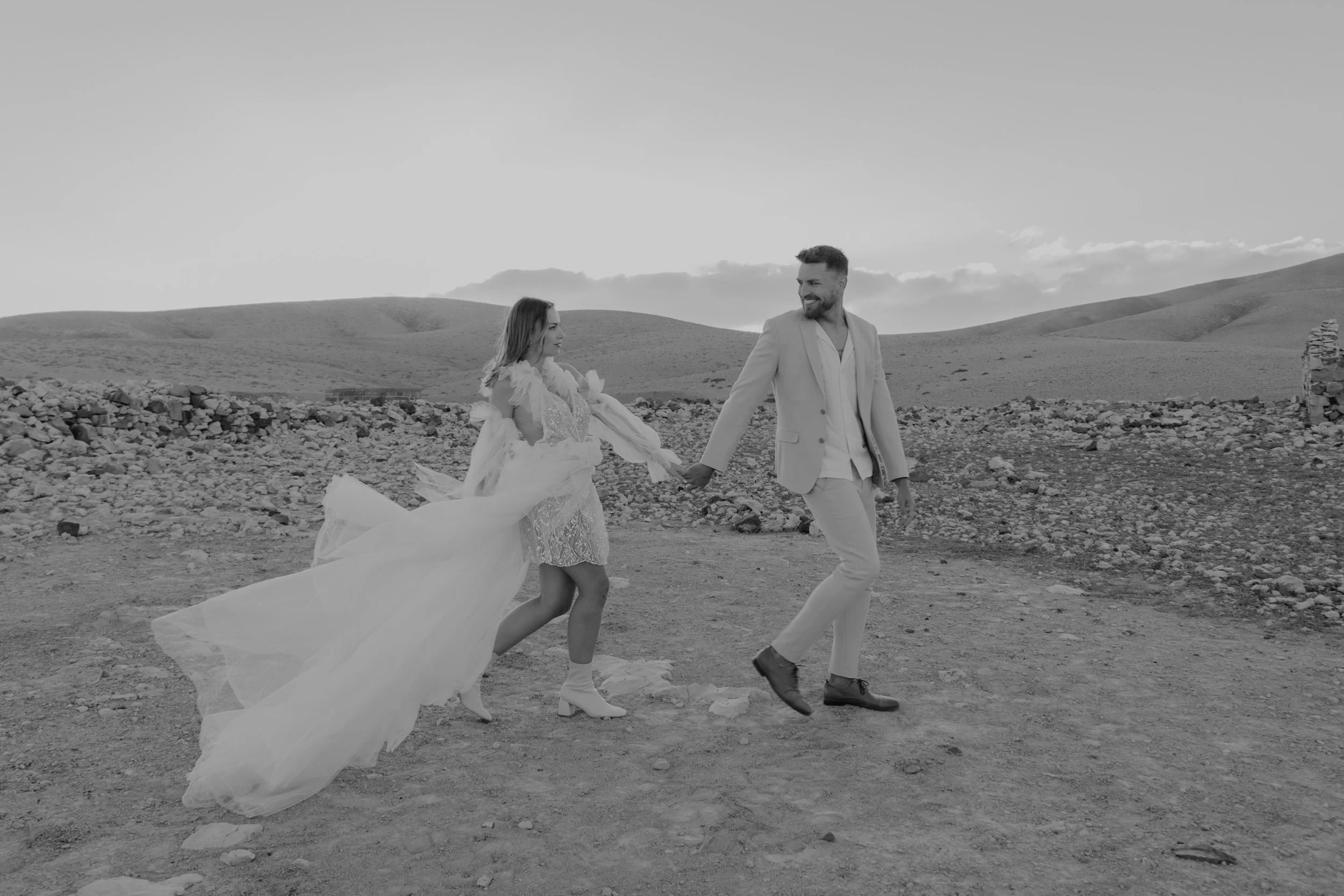 Hochzeit im Ausland – Paar läuft Hand in Hand im Sonnenuntergang durch die Wüste von Fuerteventura, Spain. 