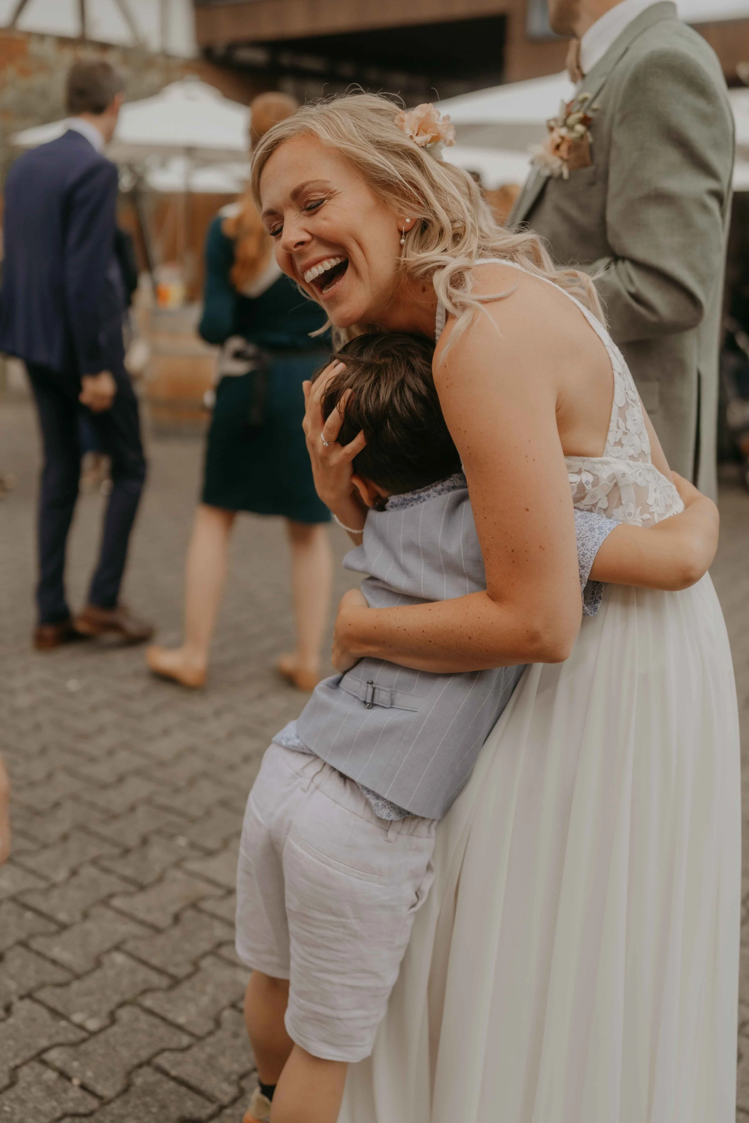 Braut und Bräutigam im Gespräch mit Gästen beim Sektempfang am Hof Café, herzliche Umarmungen voller Euphorie und Dankbarkeit.