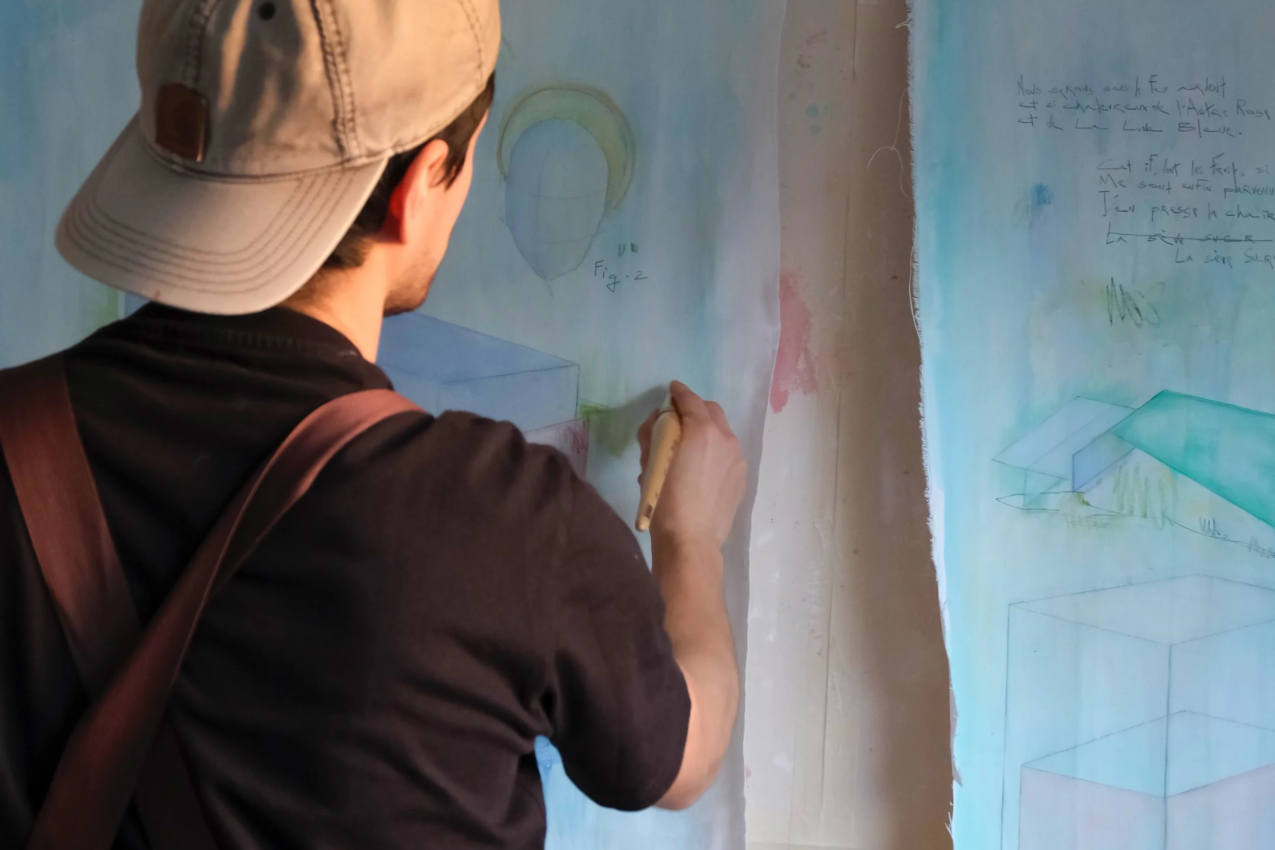 Un homme portant une casquette dessine un croquis sur un mur ou une toile. Il semble faire partie d'un processus artistique ou technique, avec des notes écrites à la main à côté, représentant un dessin ou un diagramme.