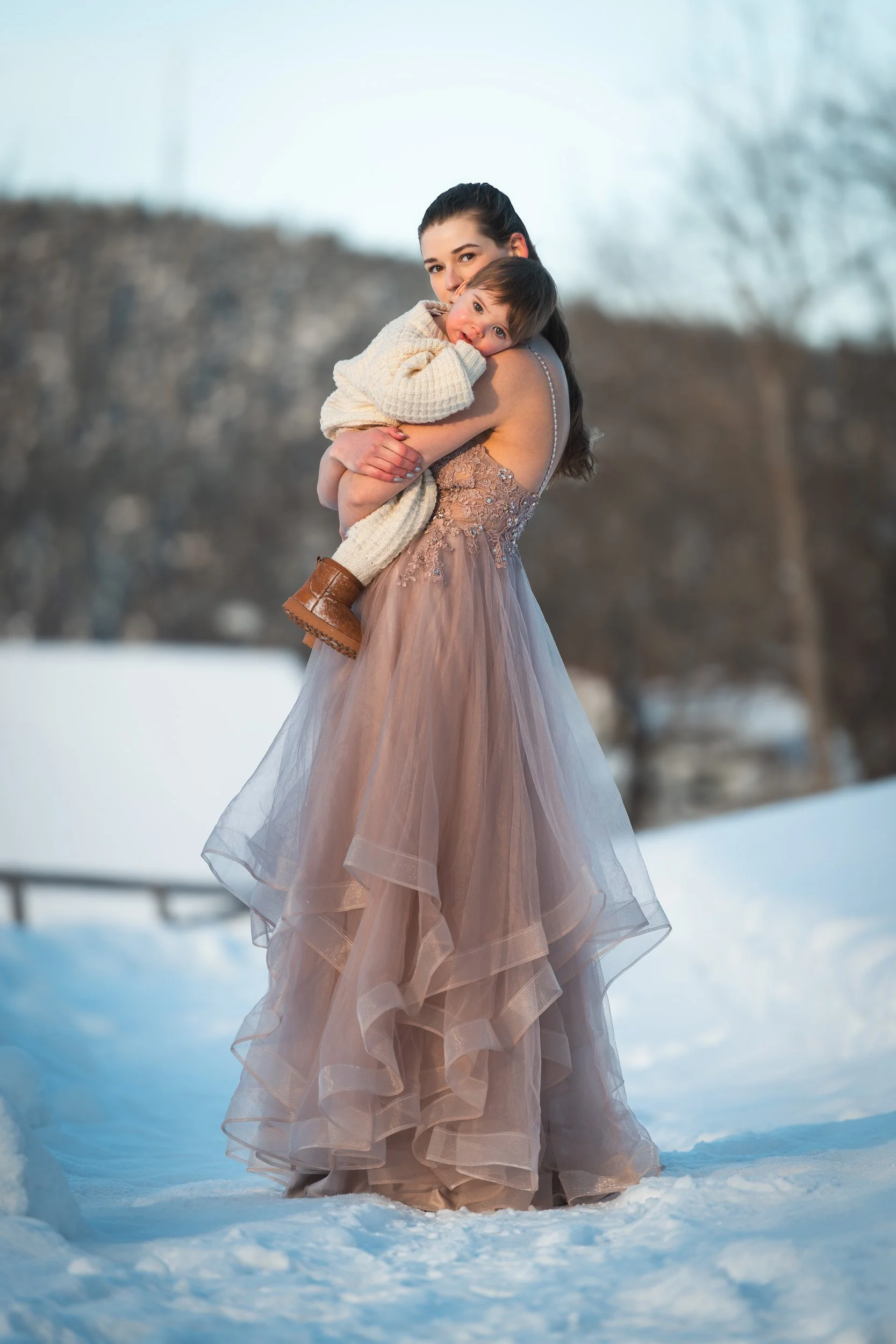 Liten gutt som hviler på skulderen til mamma. Begge to ser i kameraet. Vinterlandskap i bakgrunnen.