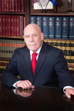 A photo of our founder, Robert J. Guendelsberger, an older, bald man in a dark pinstripe suit with a red tie sitting at a desk in front of bookshelves filled with legal or reference books.