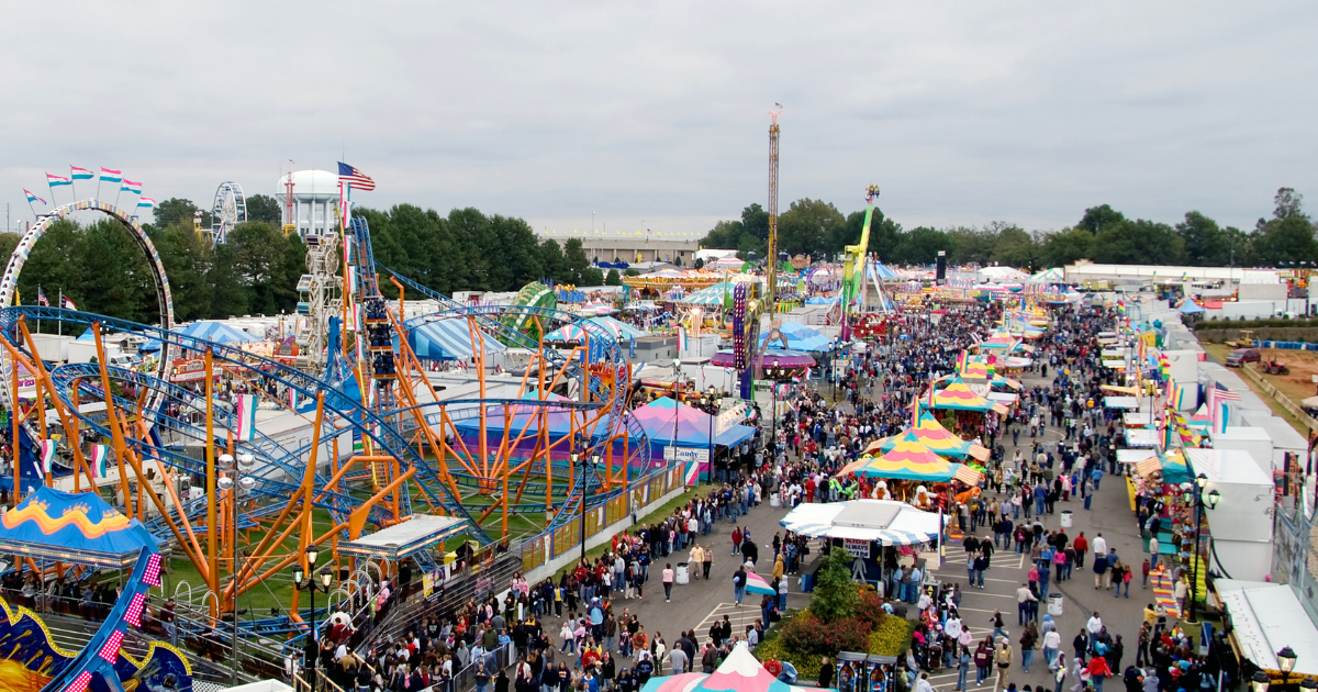 An over head picture of a big fair ground filled with people. There are rides and games and stalls.