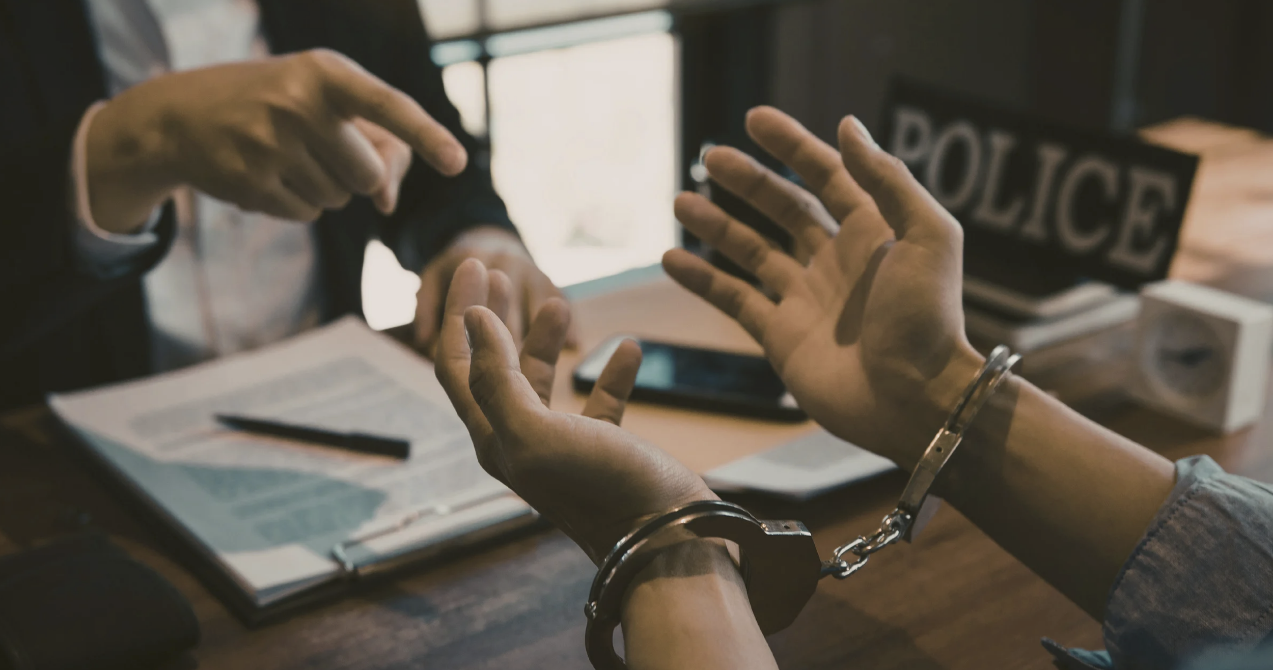 Cuffed hands over the top of a desk in a police station, upturned towards a lawyer