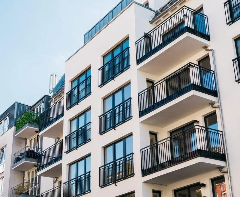 Modern white apartment building with multiple floors, each with black metal balconies and large windows.