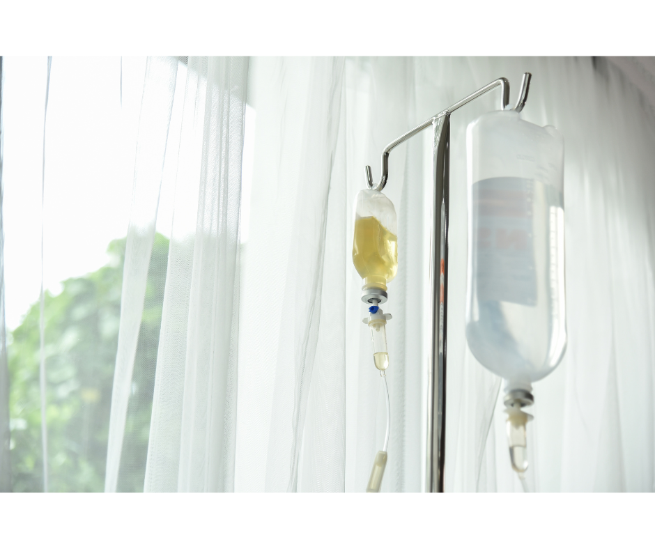 IV therapy setup at Swan Wellness Center in Tampa, FL with two infusion bags hanging on an IV stand near a window with sheer white curtains.