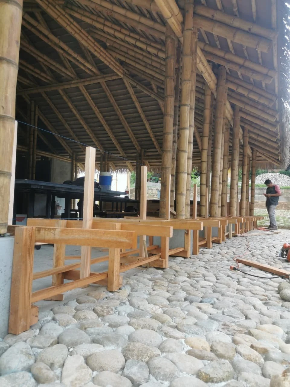Construcción de una estructura de techo de bambú con suelo de piedras y bancos de madera.
