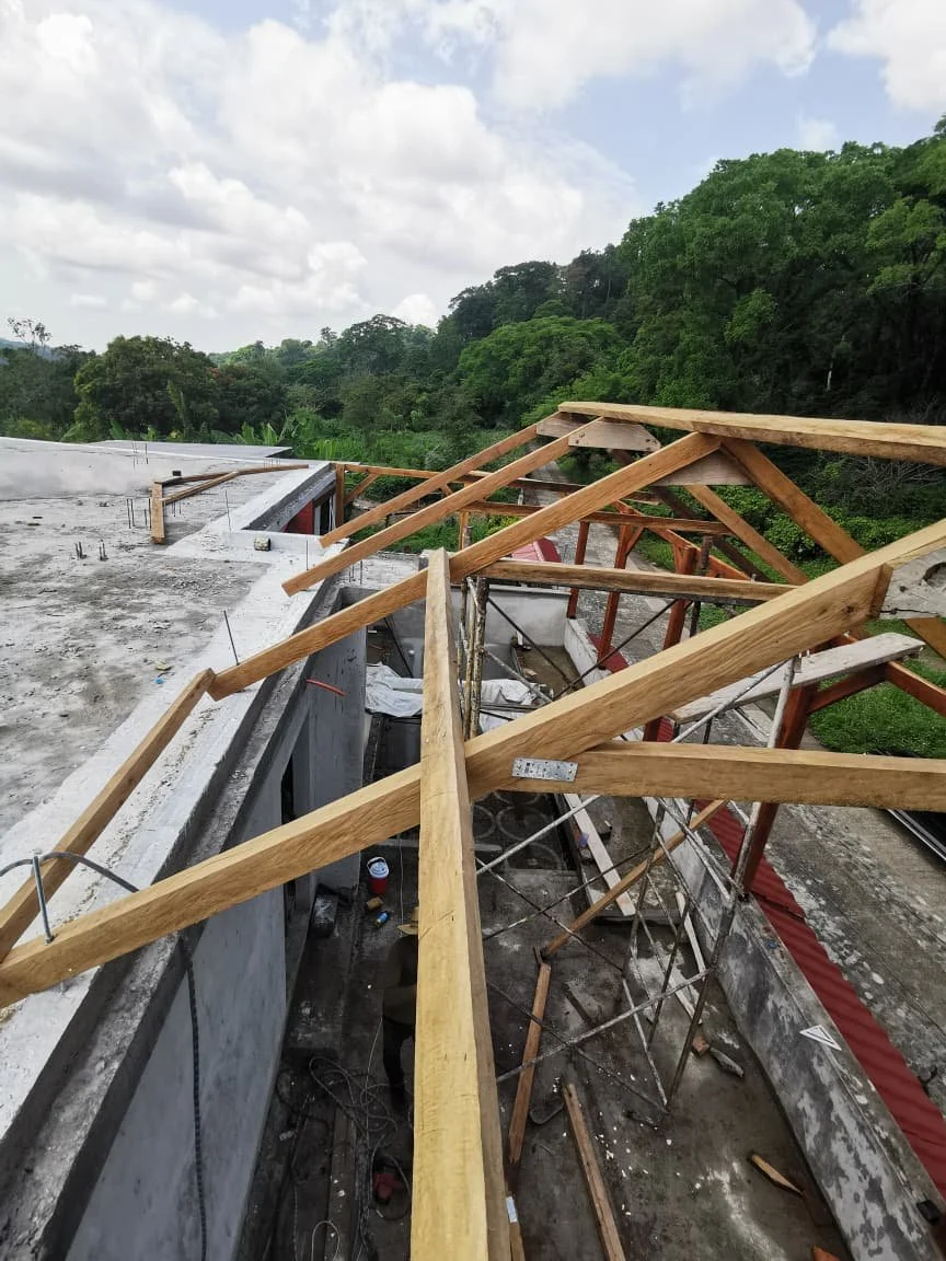 Construcción de un techo con estructura de bambú en un edificio, con herramientas y materiales de construcción, en un entorno natural.