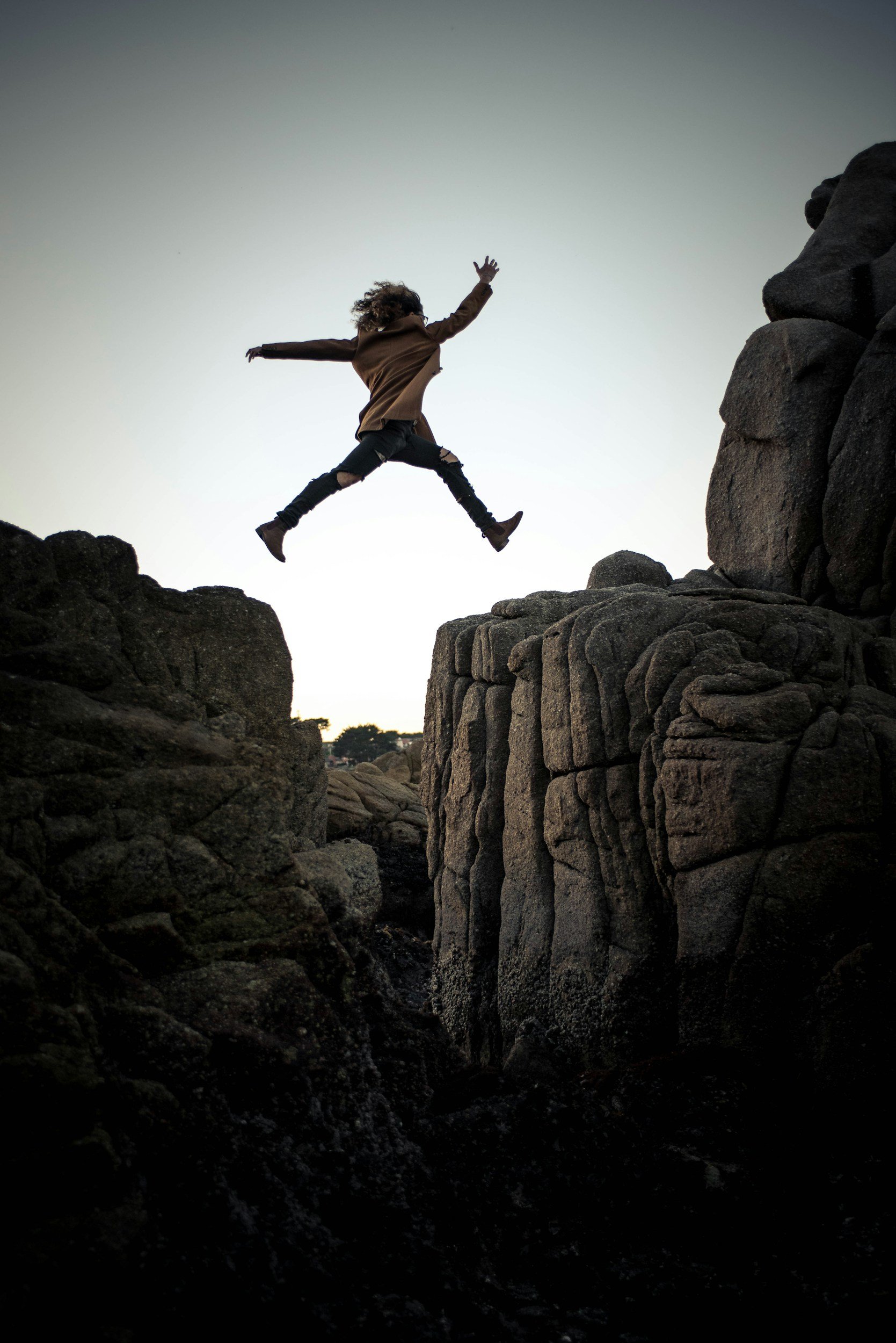 Person jumping between two rocky cliffs during sunset.