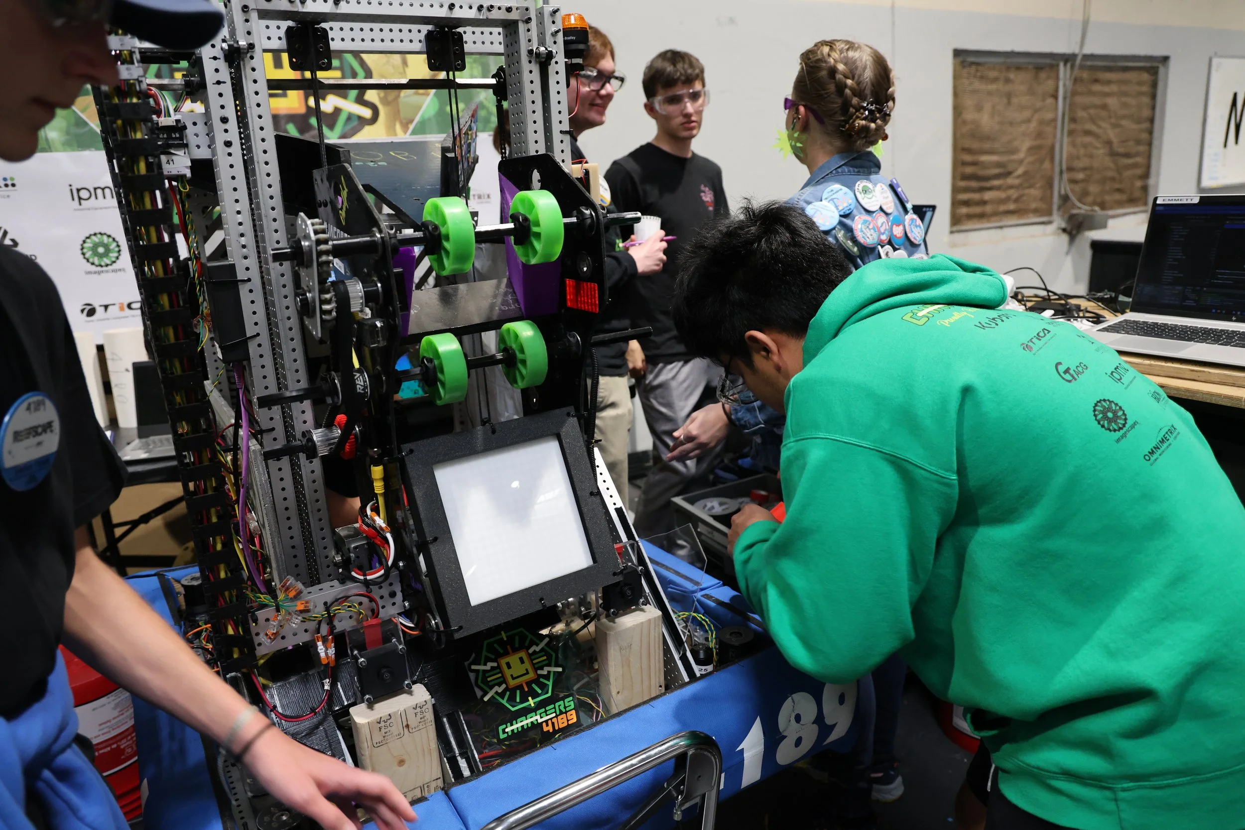 Students working on a robotics project at a competition, with a large robot and a laptop on the table.