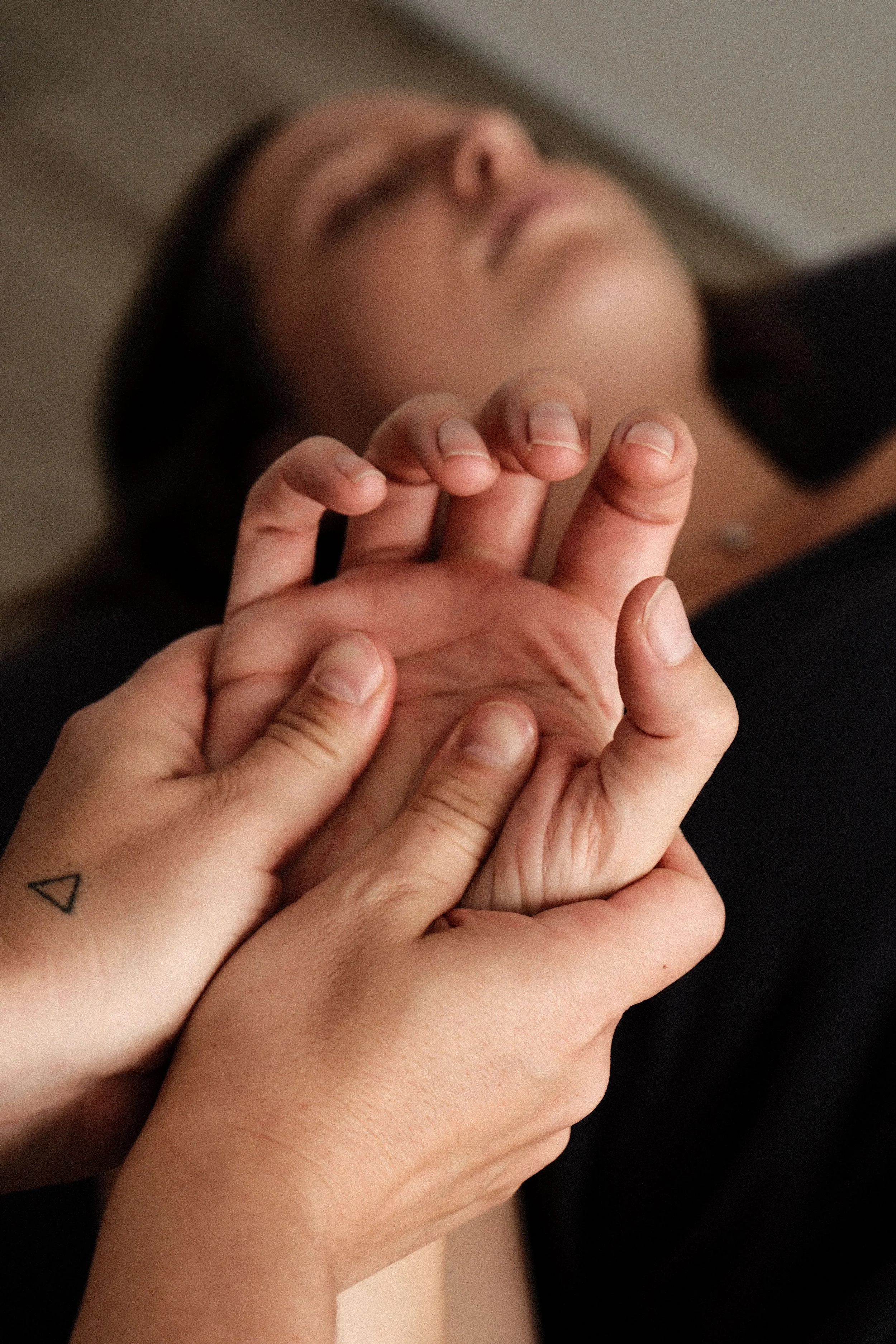 Deux mains tenant une autre main, une personne allongée en arrière, yeux fermés, semble se faire masser ou recevoir une aide.
