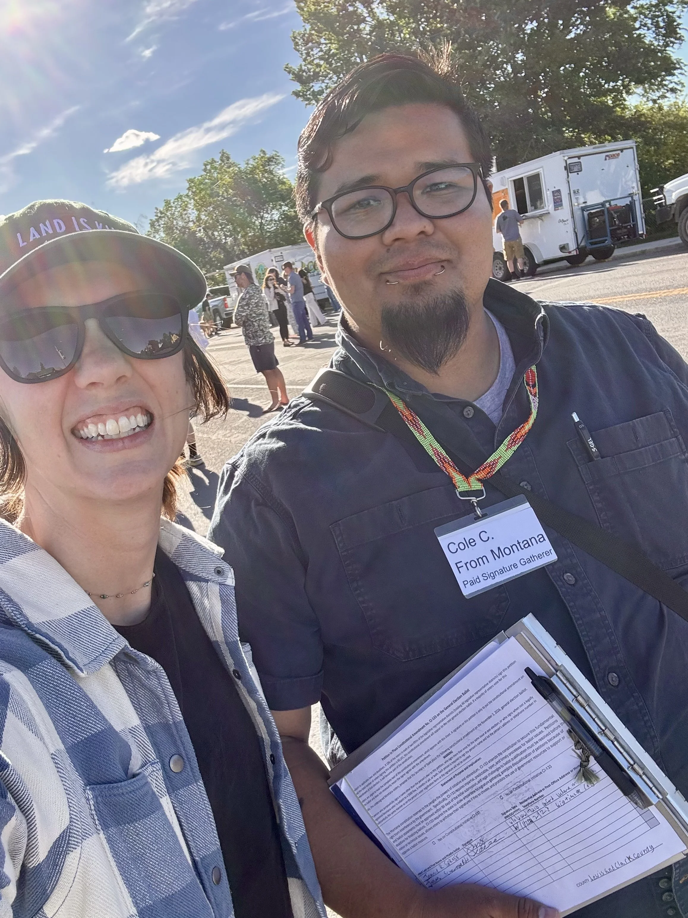 Two people pose for a selfie at a food truck fair where they are gathering signatures for CI-133